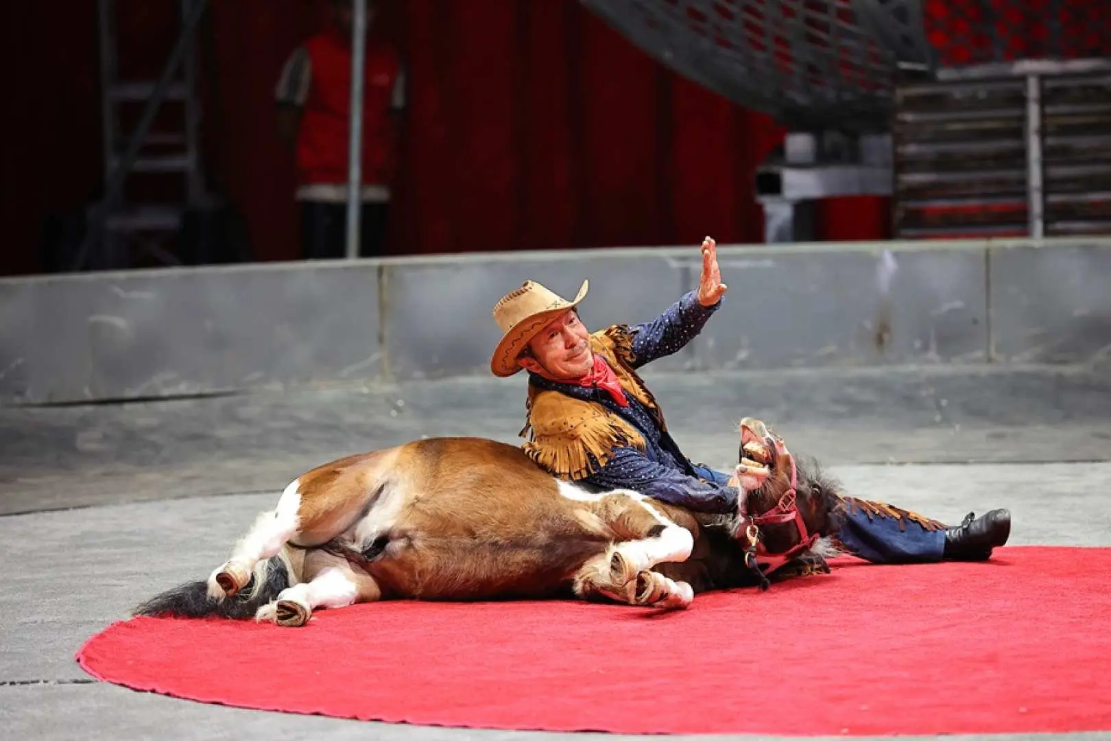A unique humorous act at Taichung Houli Crazy Horse Circus, featuring a cowboy-hatted performer sitting on a small pony lying on the ground, creating a comical interaction.