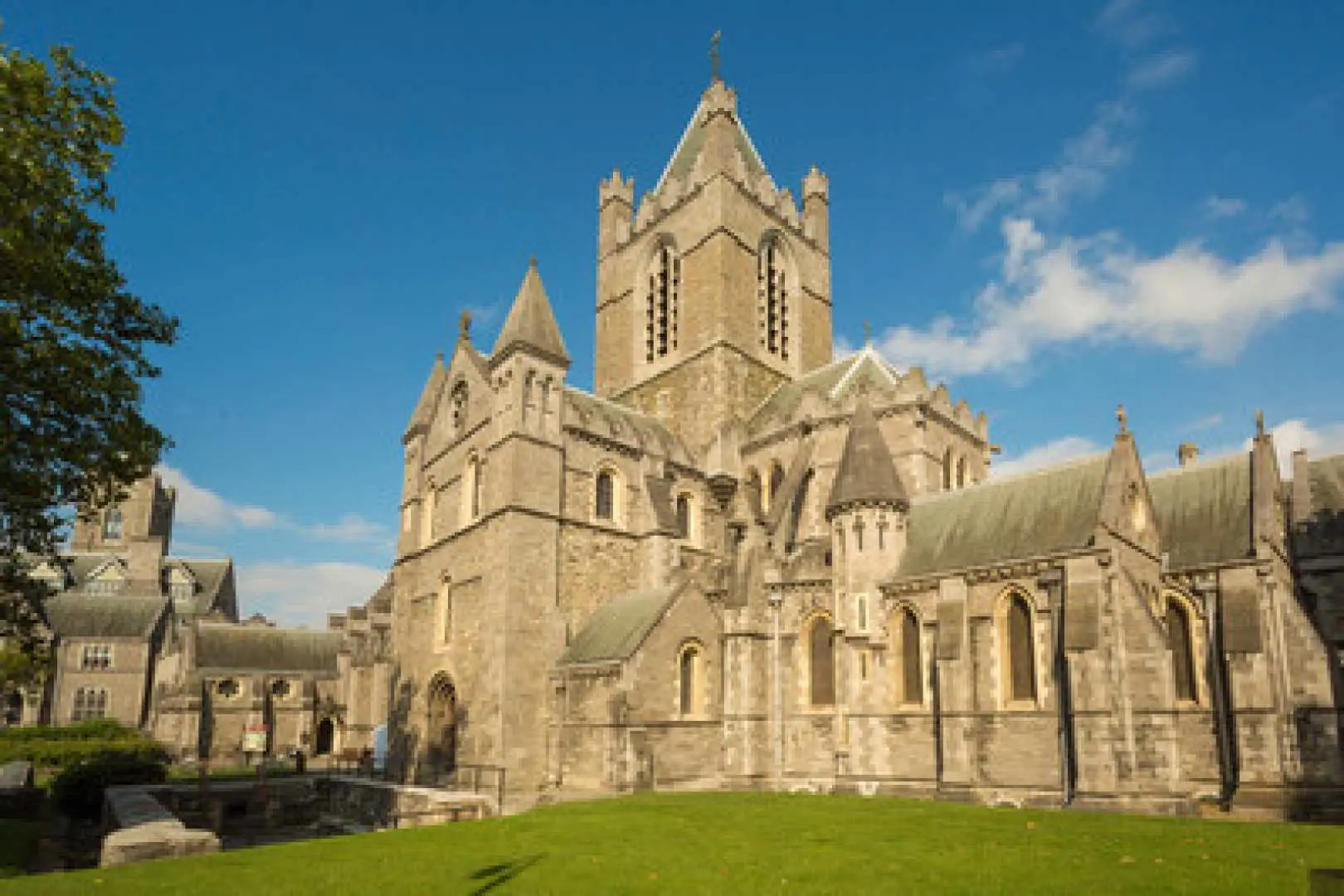 Dublin's historic Christ Church Cathedral, a grand stone edifice standing majestically under a blue sky, surrounded by lush green lawns, a key Dublin landmark.