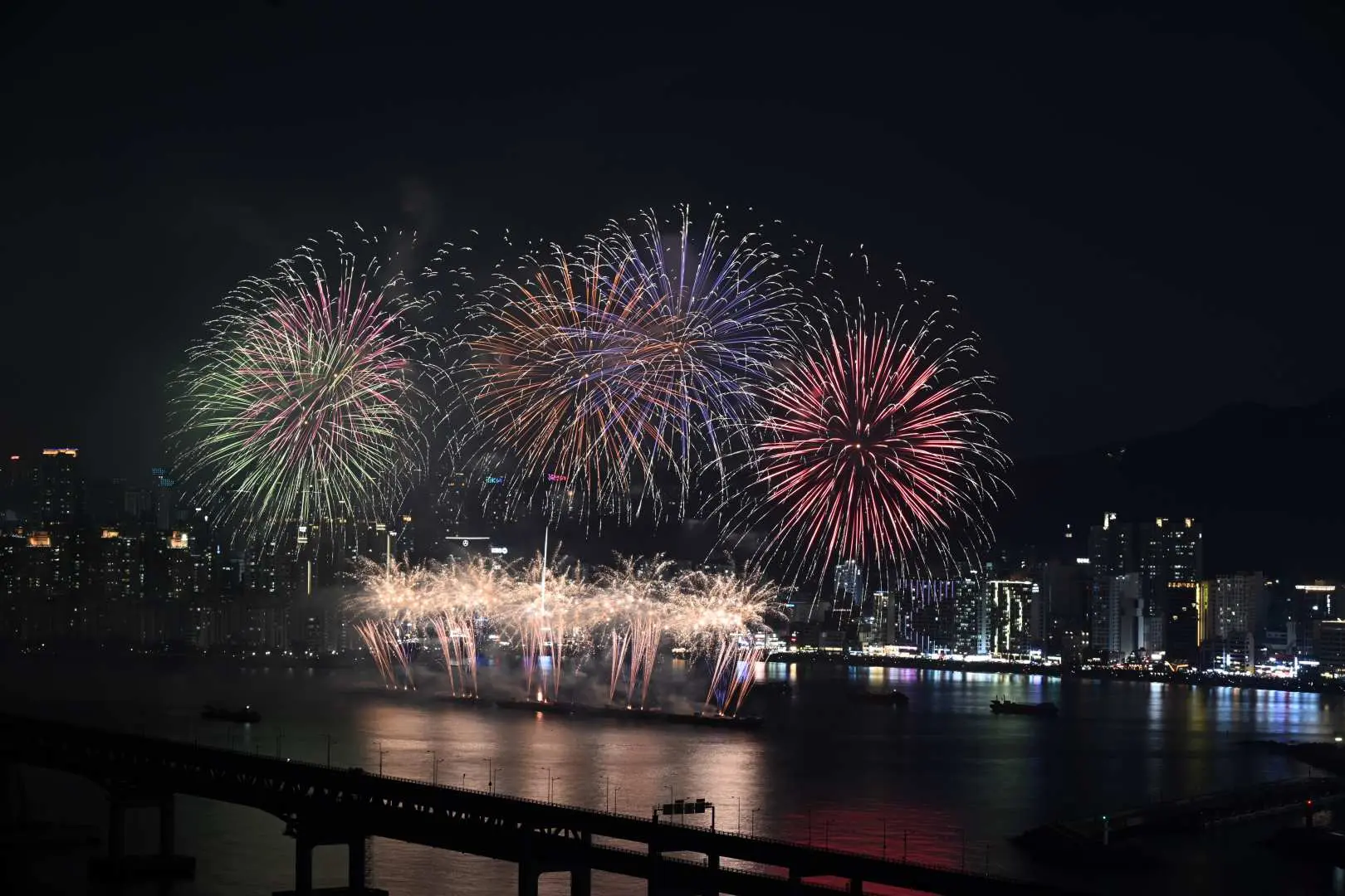 廣安大橋上方，2025釜山煙火節呈現大規模藍色、紫色與綠色煙火，照亮整個海灣與城市輪廓。