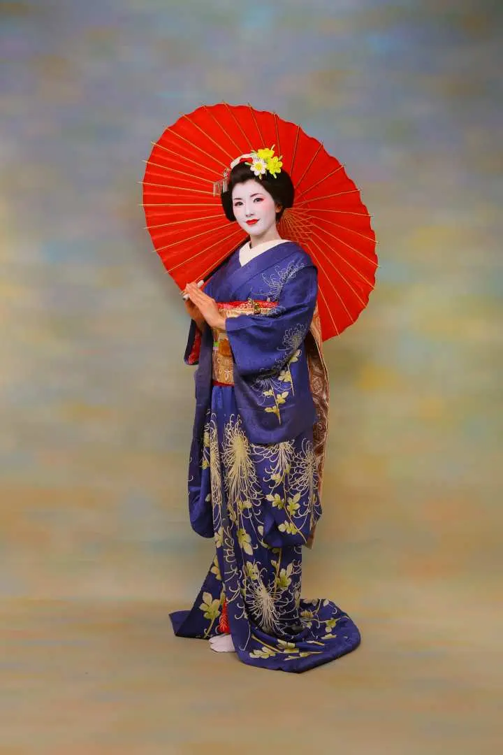 一位身著深藍色精緻舞妓和服的女士，手持紅色傳統和傘在攝影棚中擺拍，展現優雅的舞妓變身藝術照。