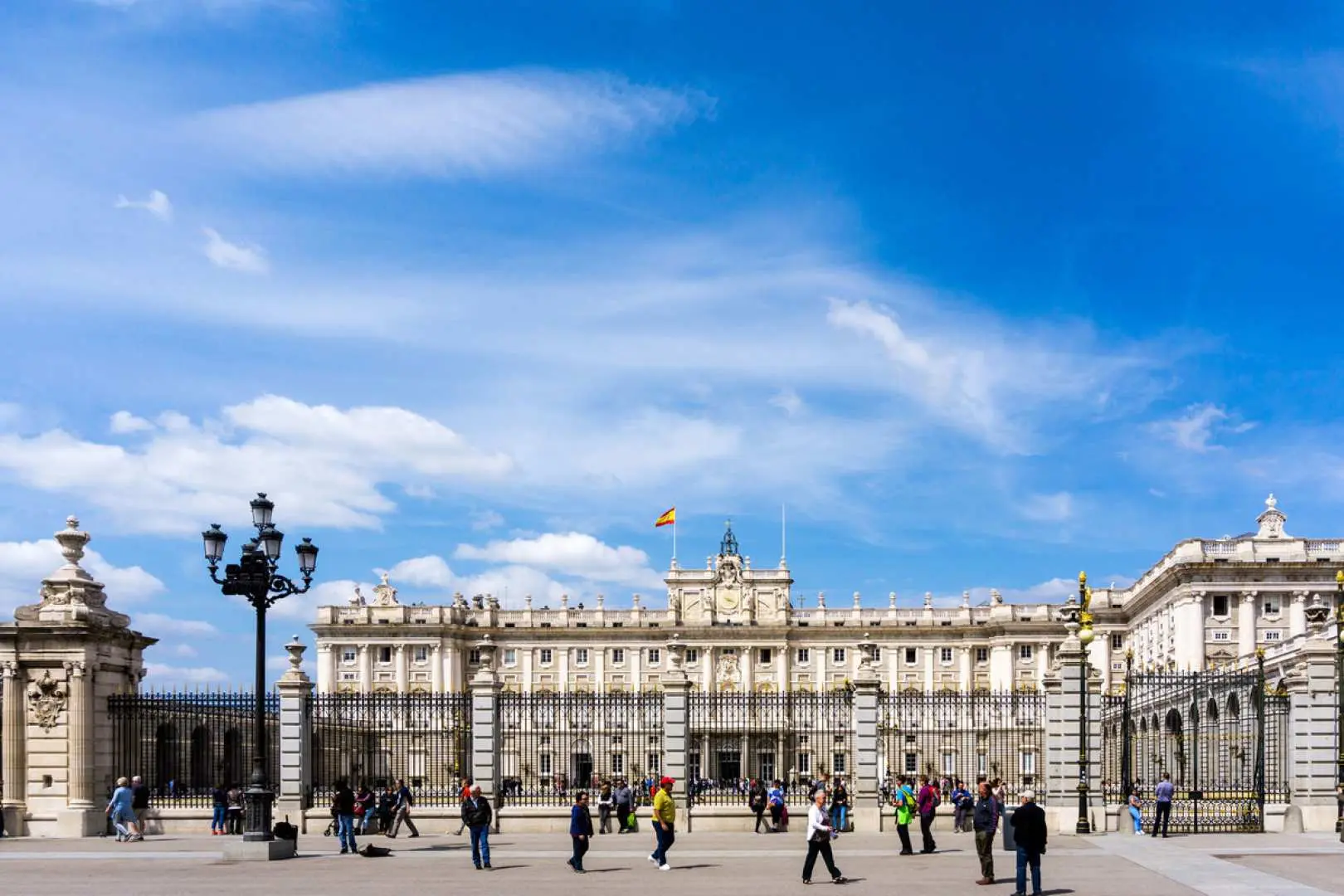 The majestic Royal Palace of Madrid (Palacio Real) under a brilliant blue sky, showcasing its grand neoclassical architecture and expansive courtyard filled with visitors, an iconic Madrid landmark.