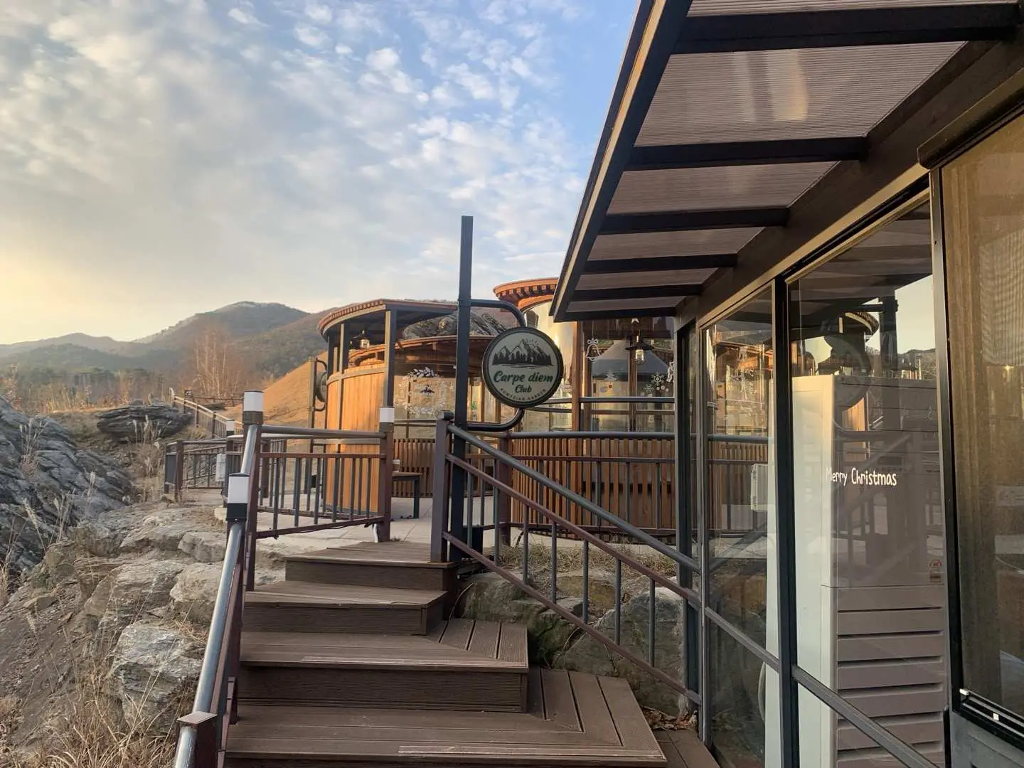 Wooden entrance building of Romijian Forest Garden in Jeongseon. Stairs guide visitors into this healing space, enhanced by serene mountain views under the warm sunset glow.