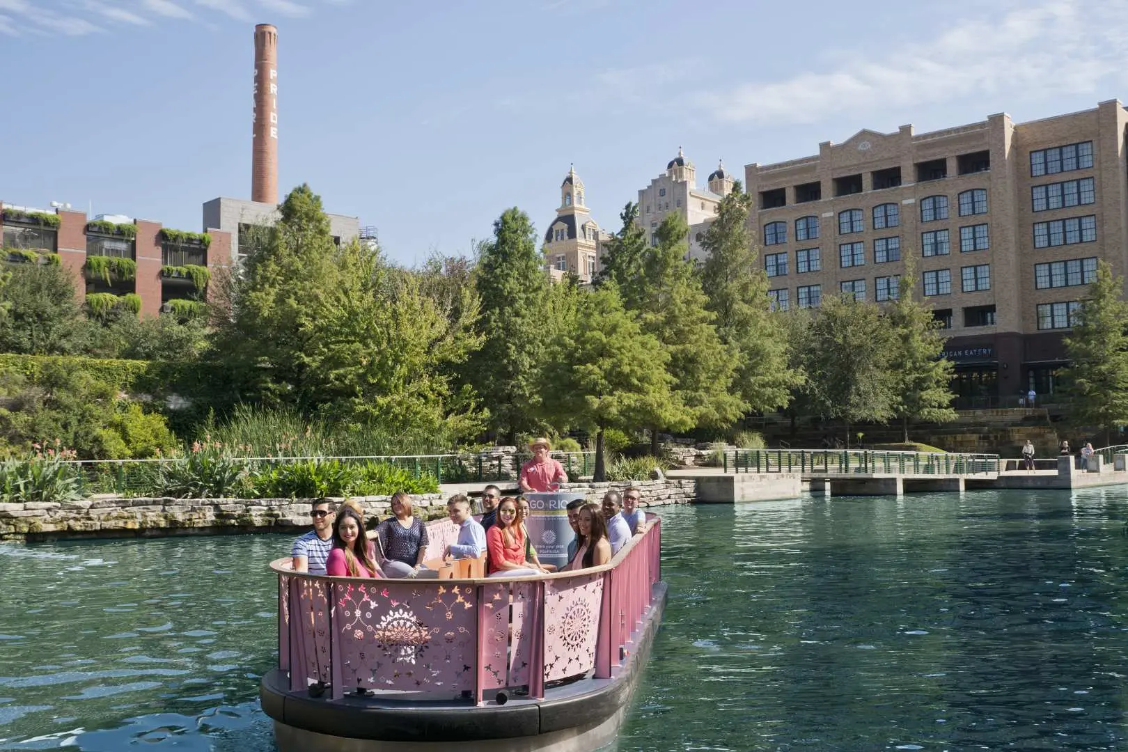 A tour boat on the San Antonio River carries visitors, cruising past unique historical buildings and green riverbanks, exploring the city's scenery with CityPASS®.
