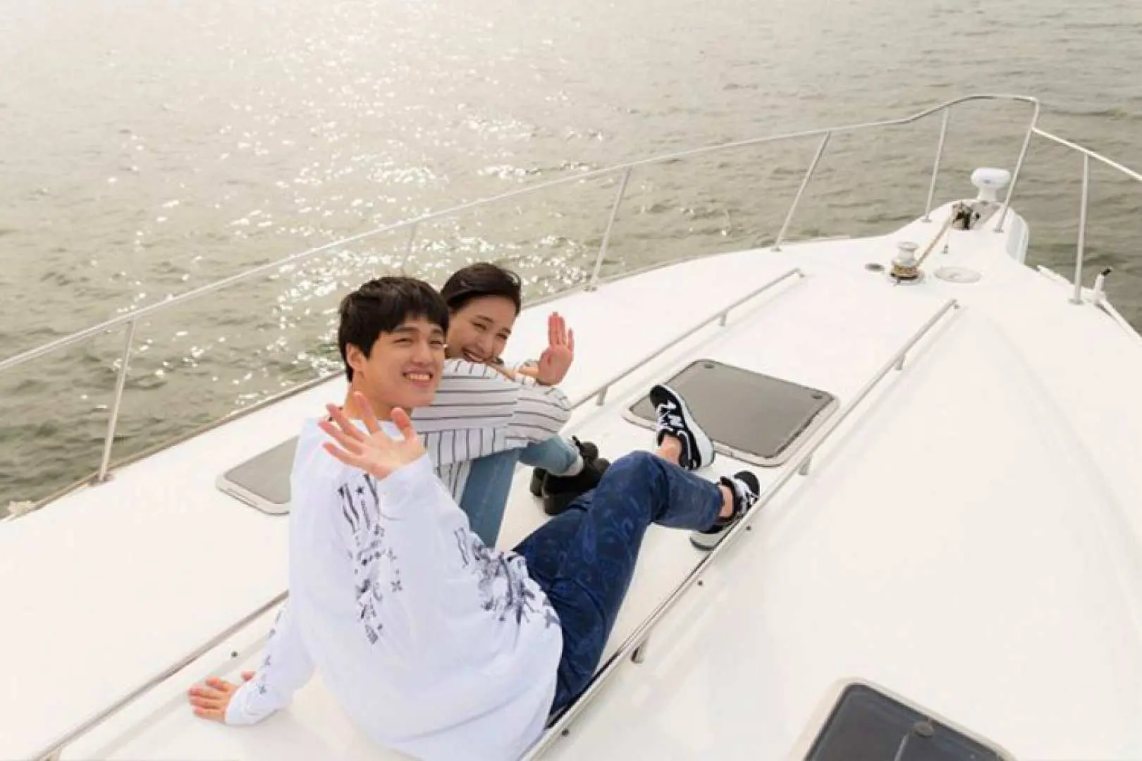 Two young people on the deck of a luxury private yacht enjoying the sunshine and beautiful Han River scenery, casually waving at the camera, experiencing a leisurely cruise.