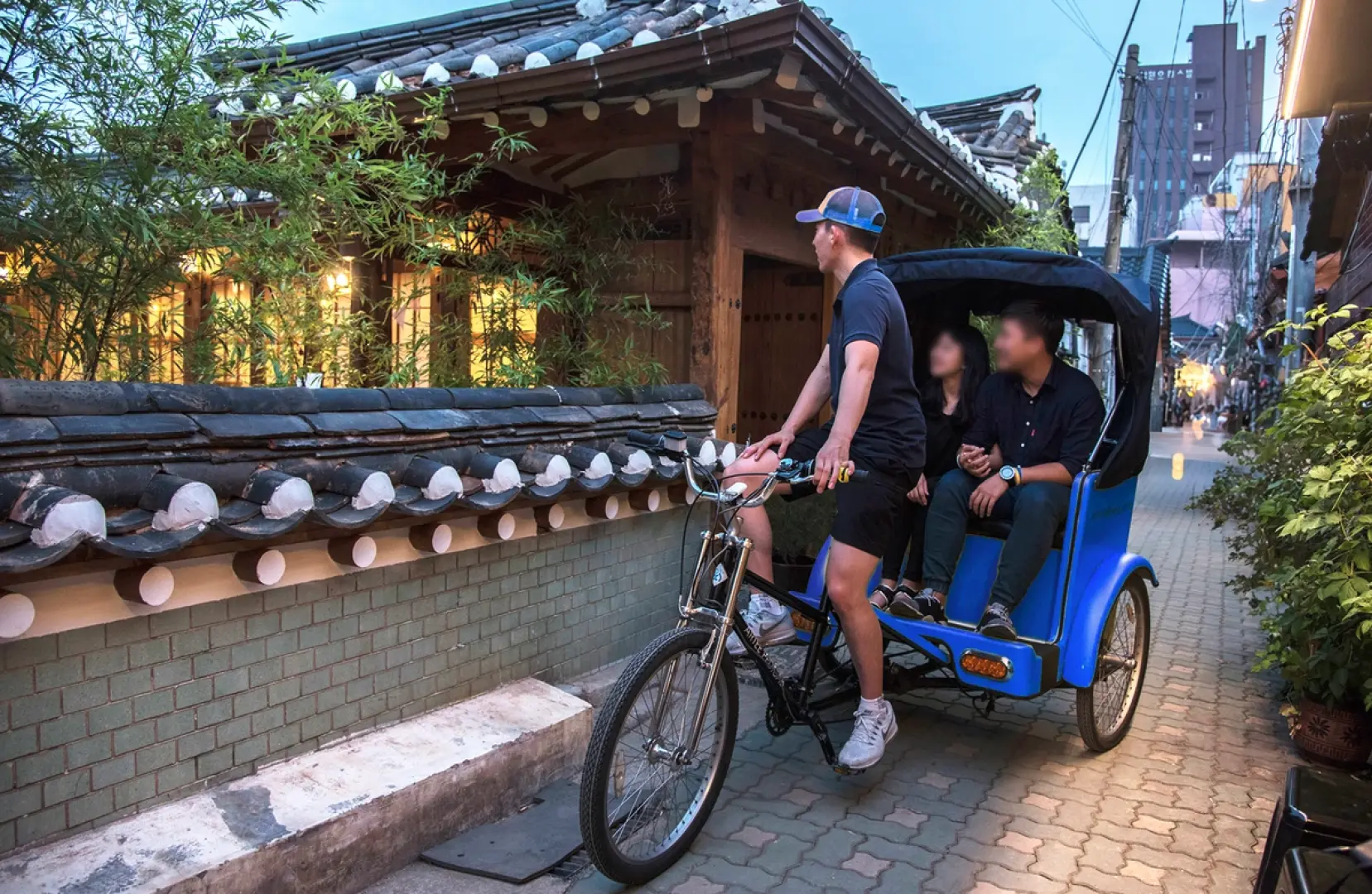 조명으로 아름답게 빛나는 전통 한옥 건물들이 늘어선 매력적인 좁은 골목길을 두 명의 방문객을 태운 인력거가 지나가며, 인사동 또는 익선동의 독특한 밤 분위기를 담은 모습.