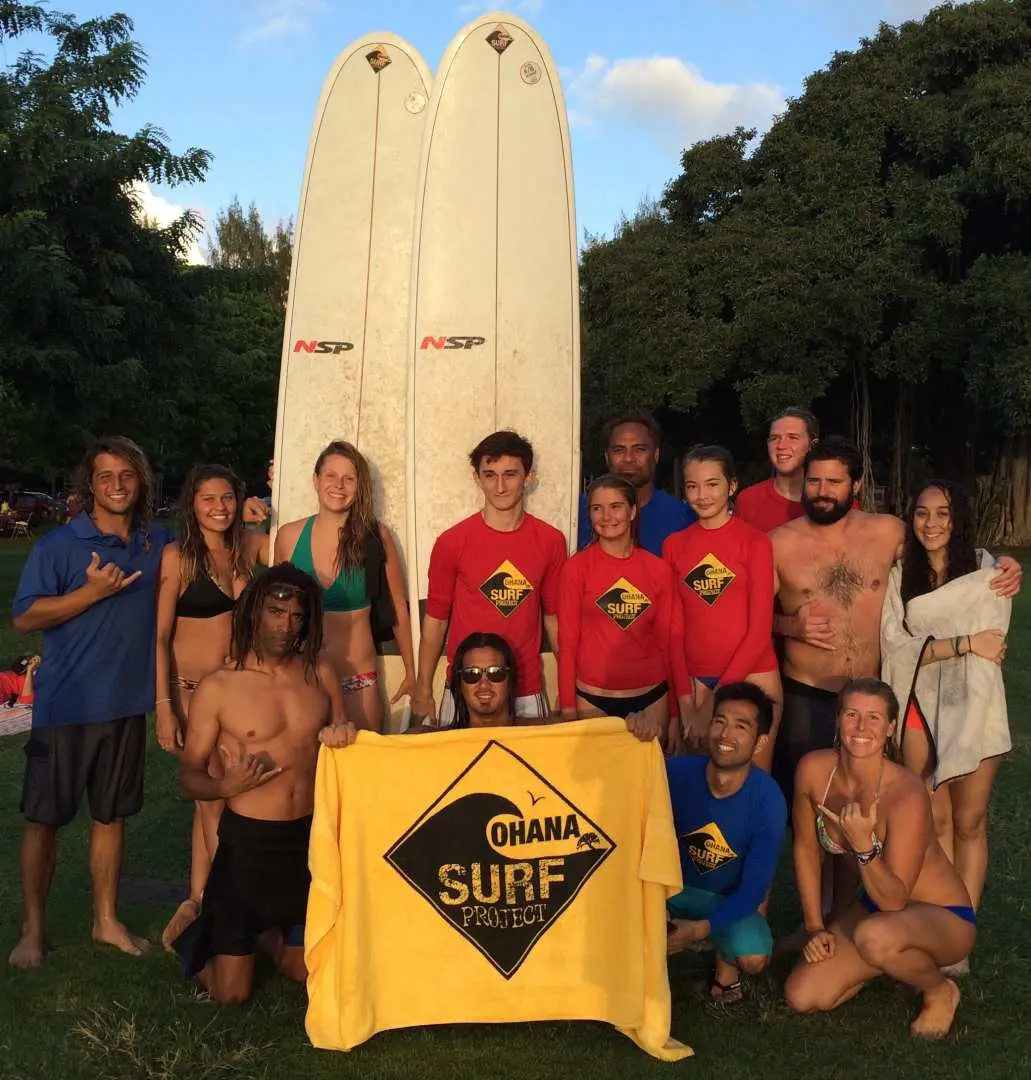 A diverse group of students and instructors posing for a joyful group photo after their surfing lesson at Hawaii's Waikiki Beach, showcasing camaraderie and fun.