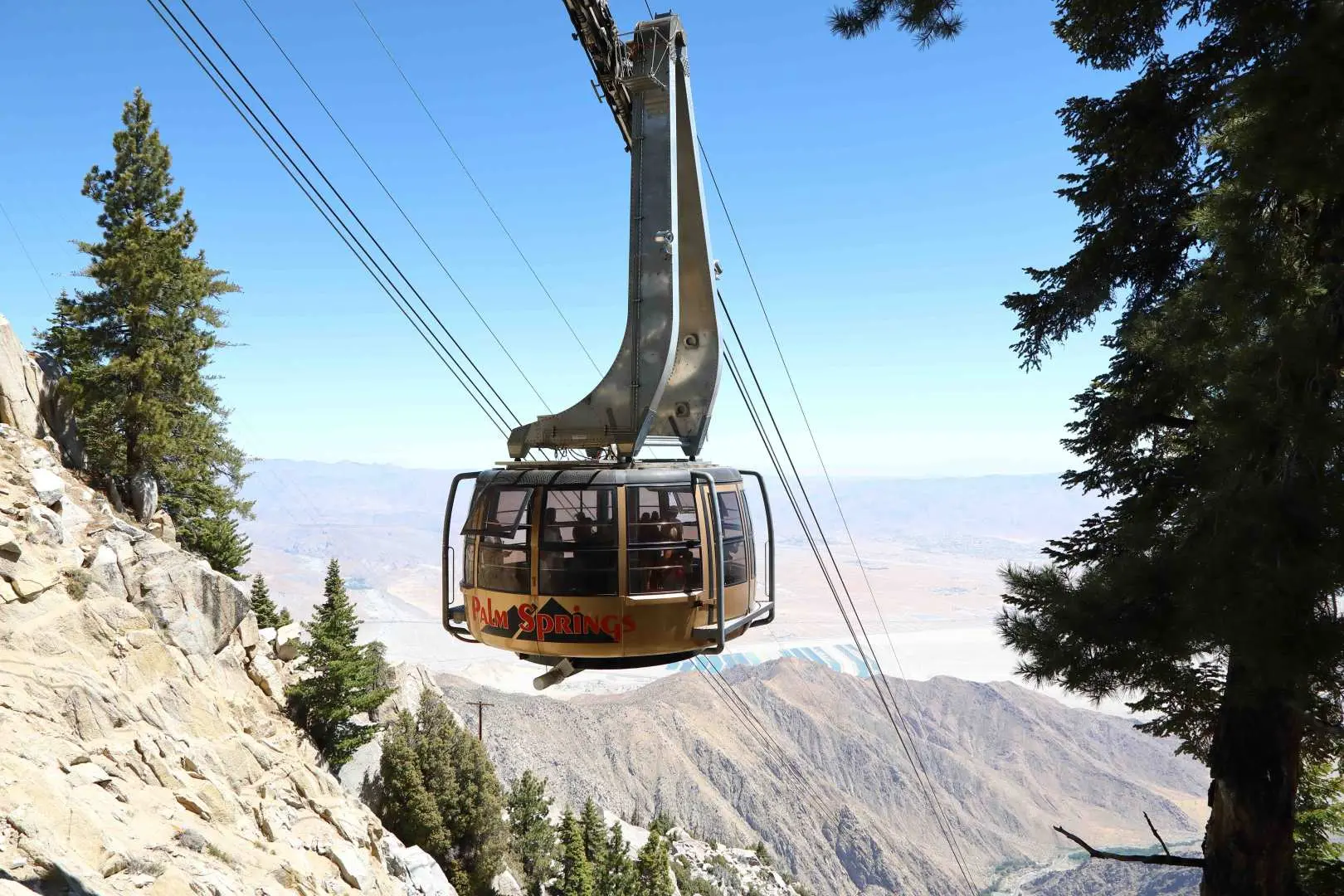 The transparent rotating car of the Palm Springs Aerial Tramway ascends toward San Jacinto Peak under a clear blue sky, offering expansive panoramic views of the Sonoran Desert.