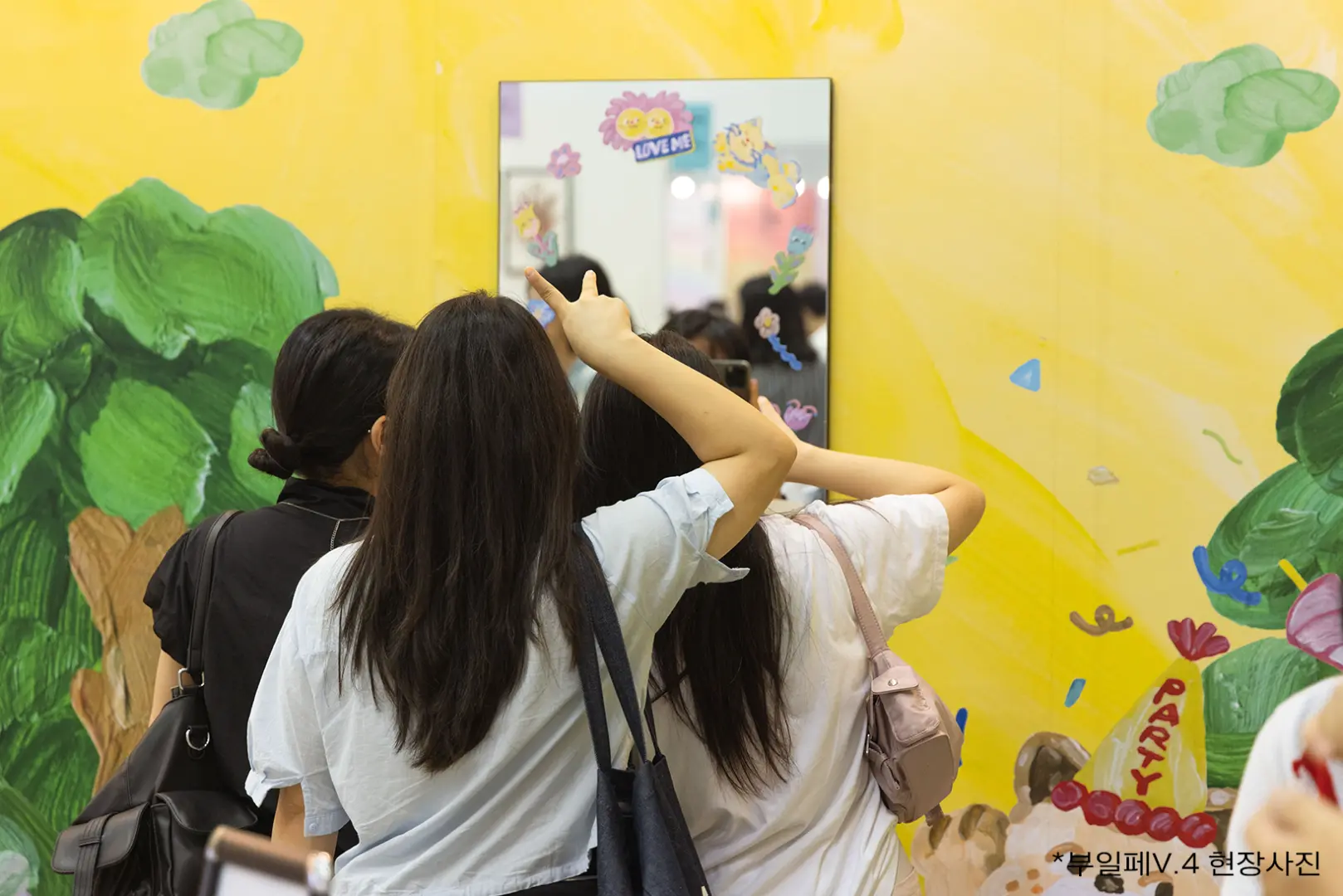 Visitors enjoying an immersive art experience at Busan Illustration Fair V.6's interactive art installation, looking into a mirror against a vibrant, colorful backdrop.