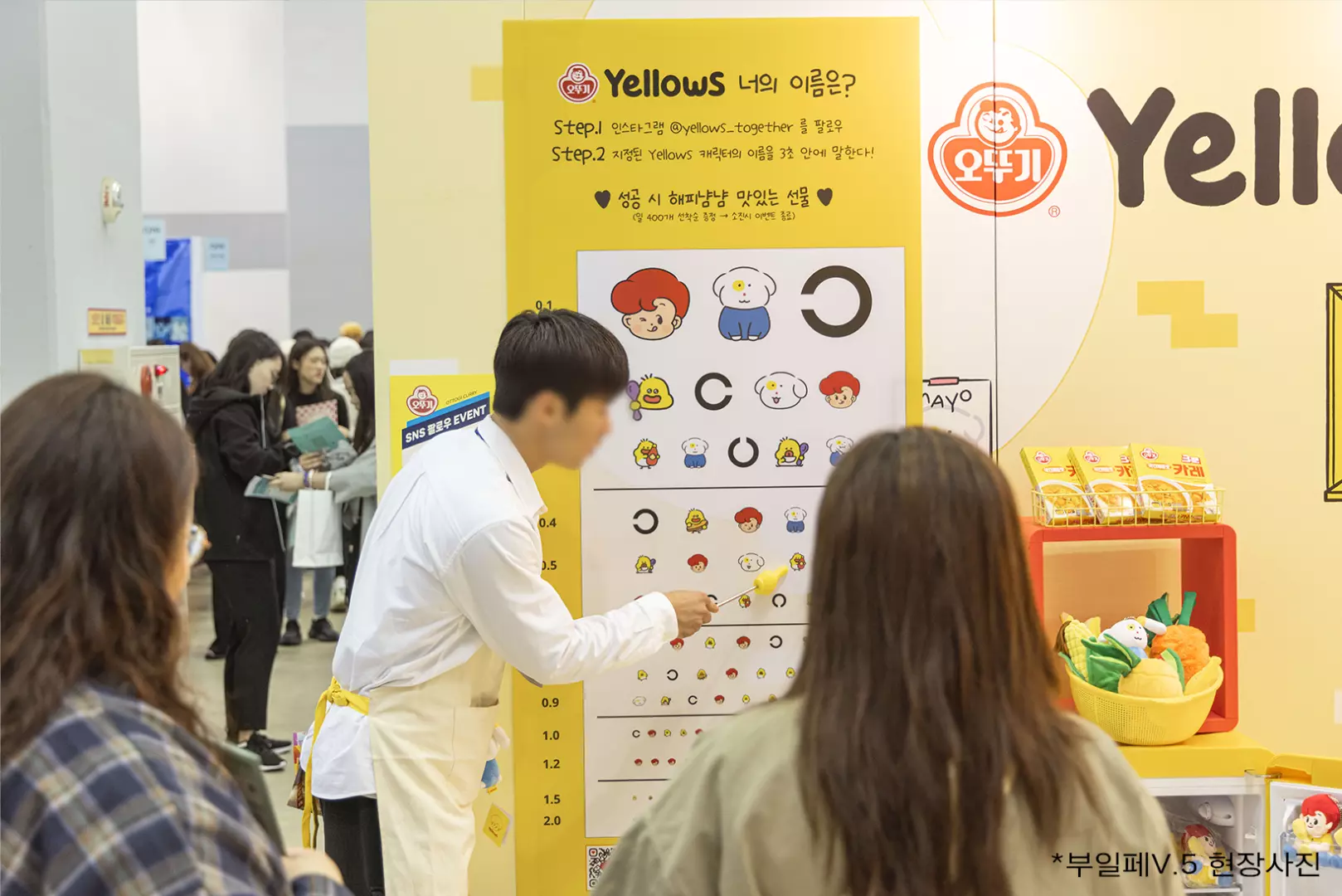 Staff guiding visitors through a fun eye chart-style illustration experience at the interactive YELLOS booth during the Busan Illustration Fair V.6.