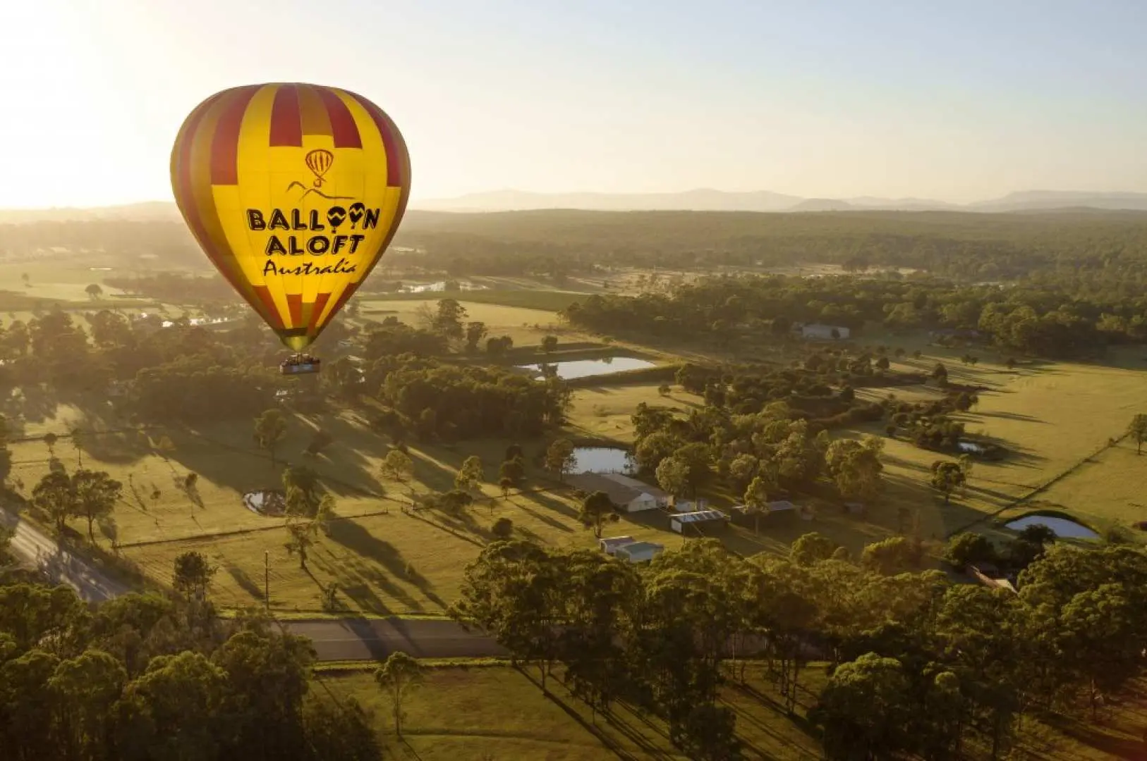 澳大利亚猎人谷热气球飞行，印有“BALLOON ALOFT Australia”字样的热气球，在金色的阳光下飘过绿色田野、树林和池塘。