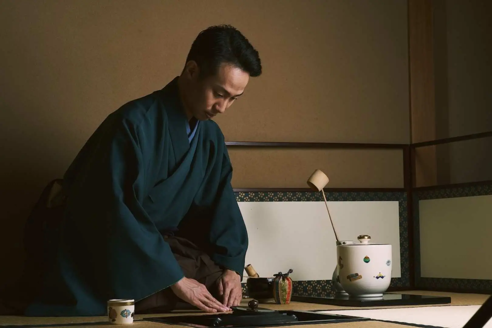 大阪の静かな茶室で、伝統的な着物を着た茶道の達人が畳の上で本格的な日本茶道の一工程を丁寧に披露しています。