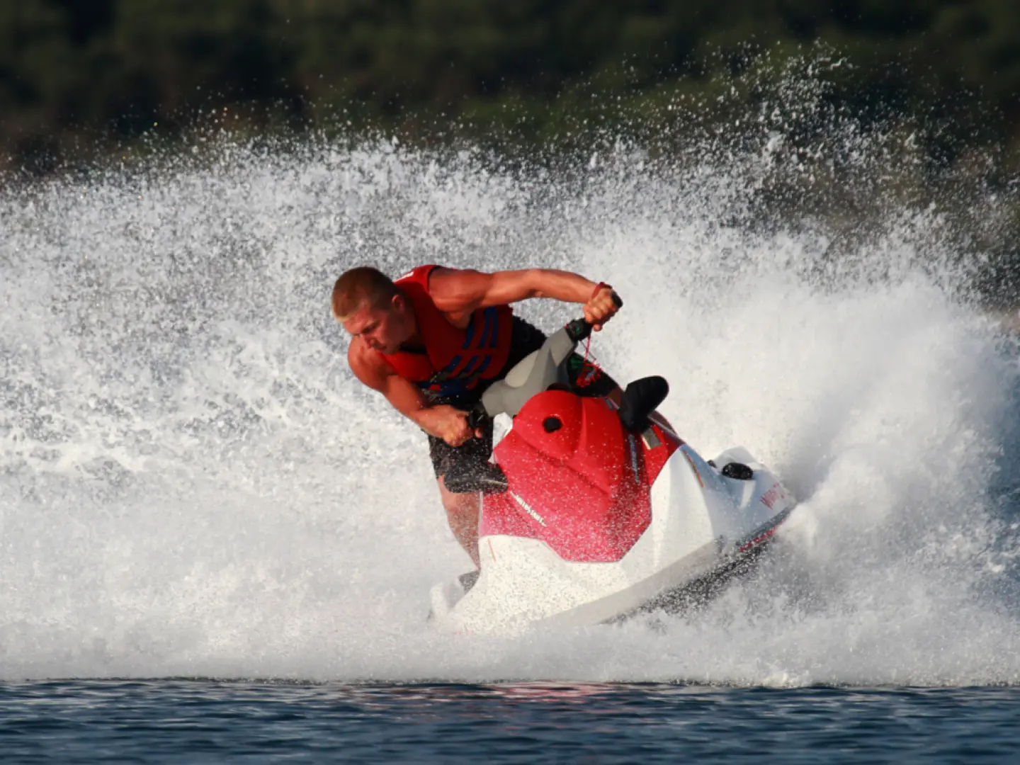 A man in a life vest skillfully steers a red and white jet ski through a sharp turn at Pattaya Beach, sending water spraying, experiencing the ultimate thrill of high-speed water riding.