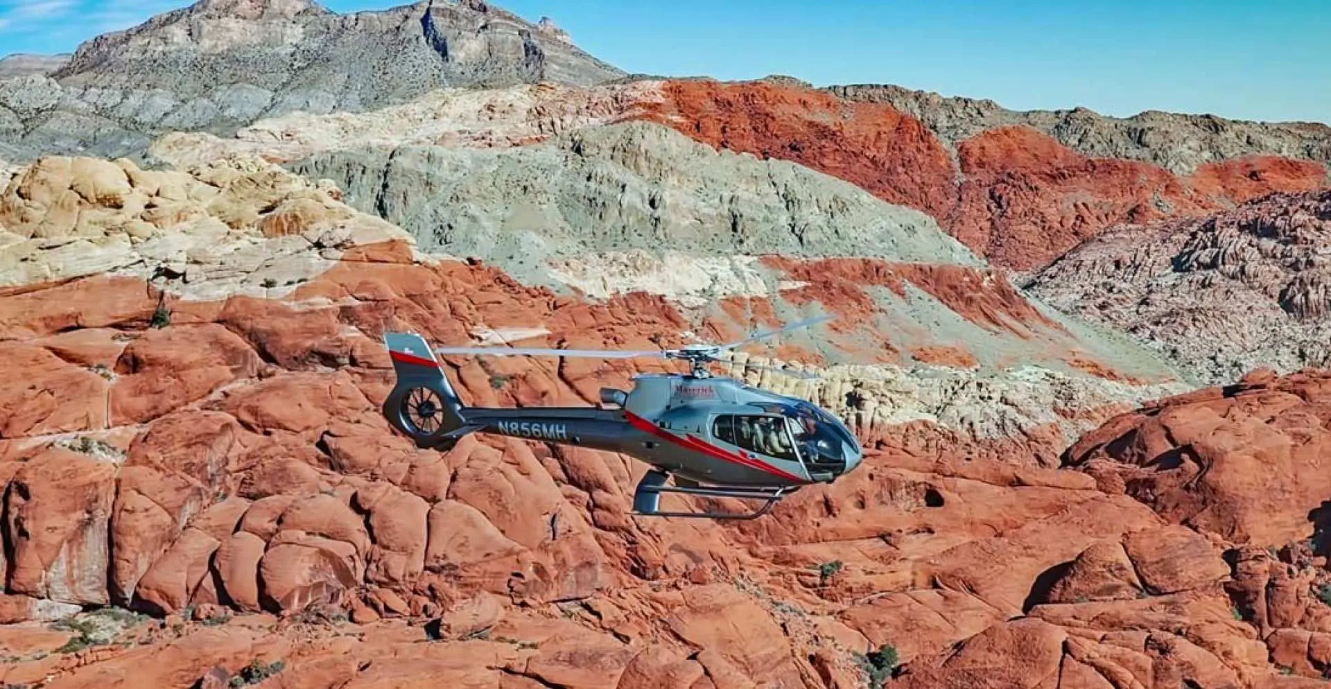 A helicopter flying over the stunning red rock formations of Red Rock Canyon in Las Vegas, showcasing the magnificent natural landscape.