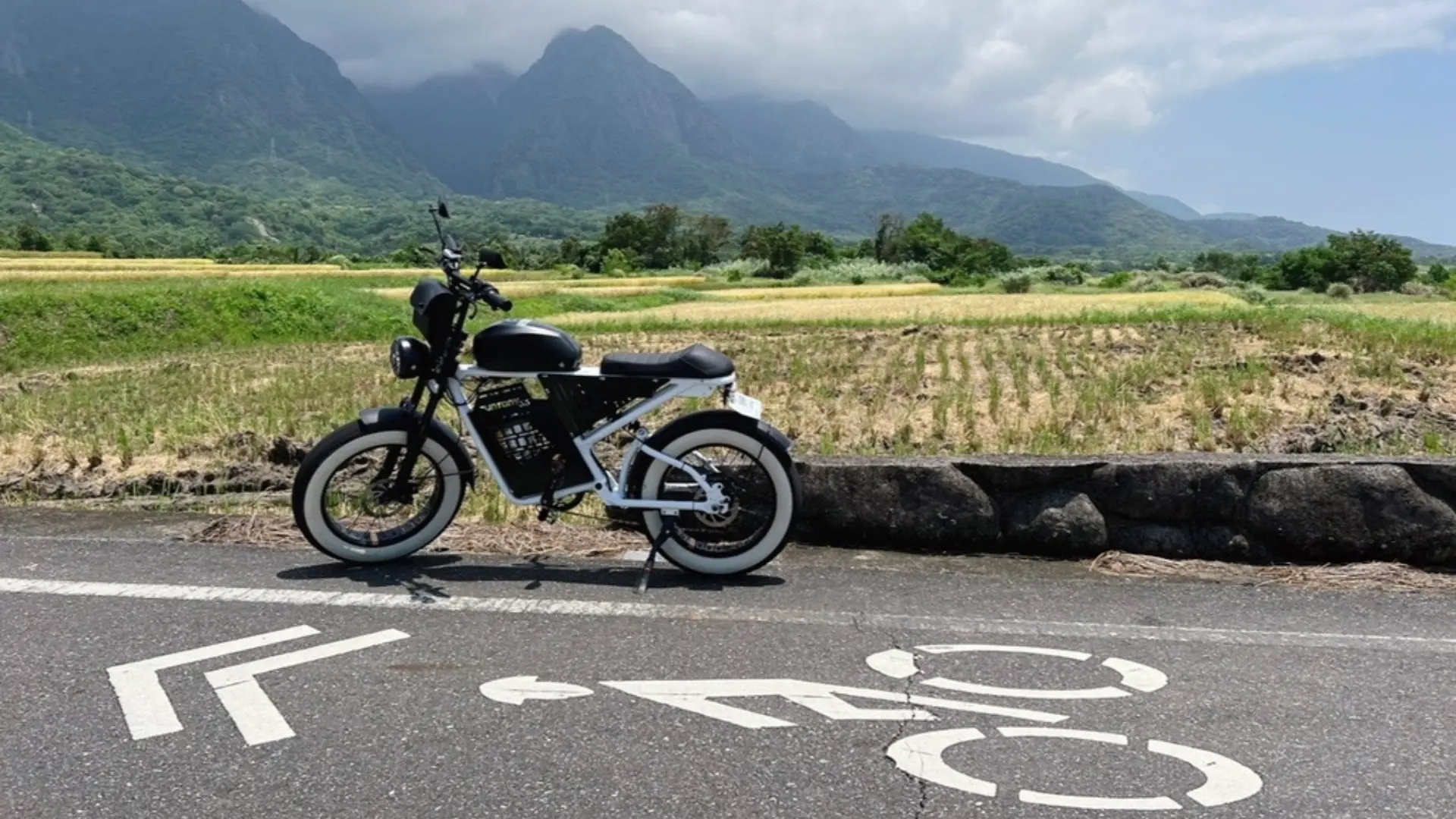 Pingtung Kenting Slow Bike electric-assisted bicycle parked on a rural road, with majestic mountains and lush rice fields in the background, perfect for slowly exploring Hengchun's natural beauty.