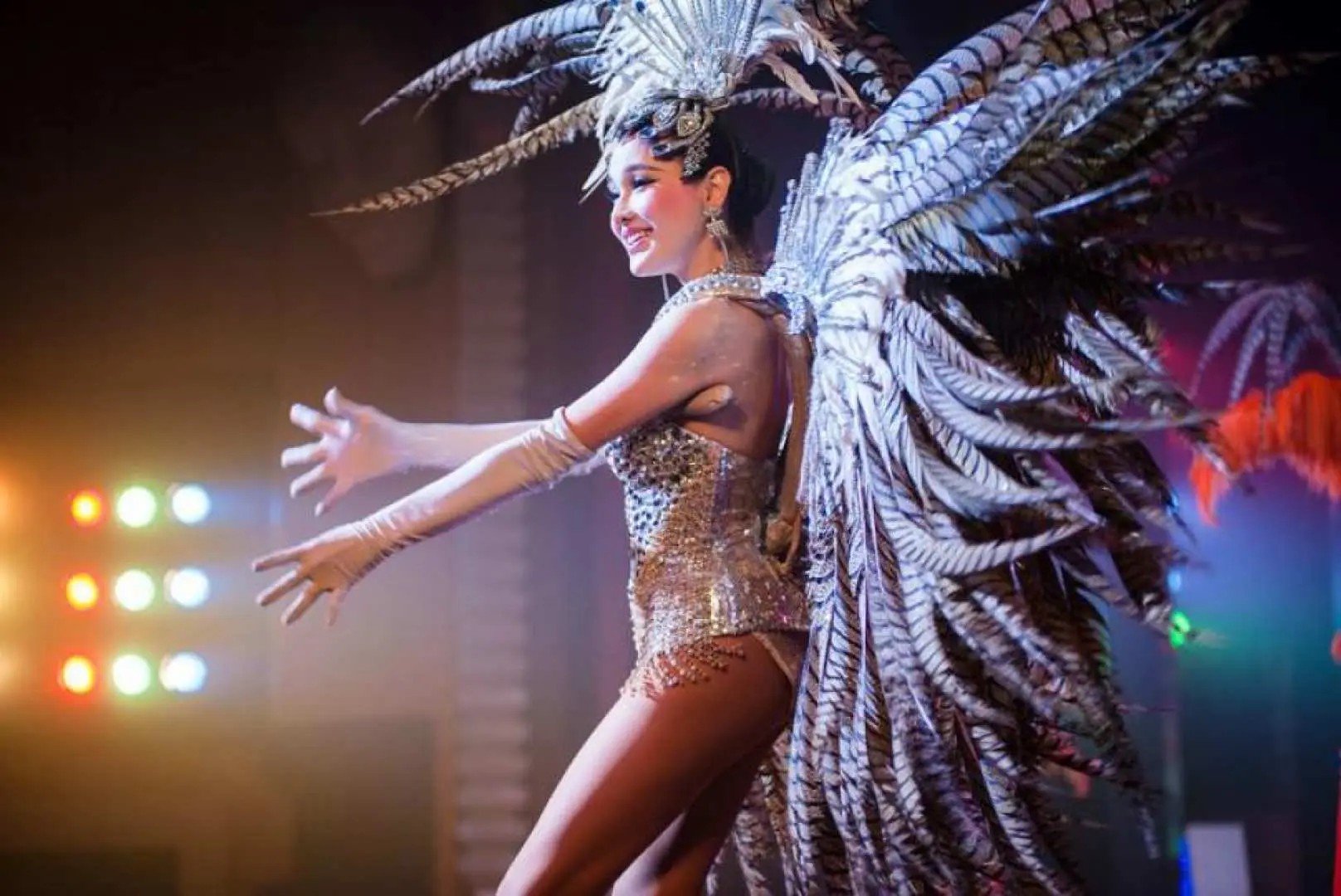 Một nghệ sĩ biểu diễn Alcazar Cabaret tại Pattaya đang mỉm cười, lộng lẫy trong trang phục showgirl lấp lánh với đôi cánh lông vũ tráng lệ, trình diễn vũ điệu đẳng cấp thế giới.