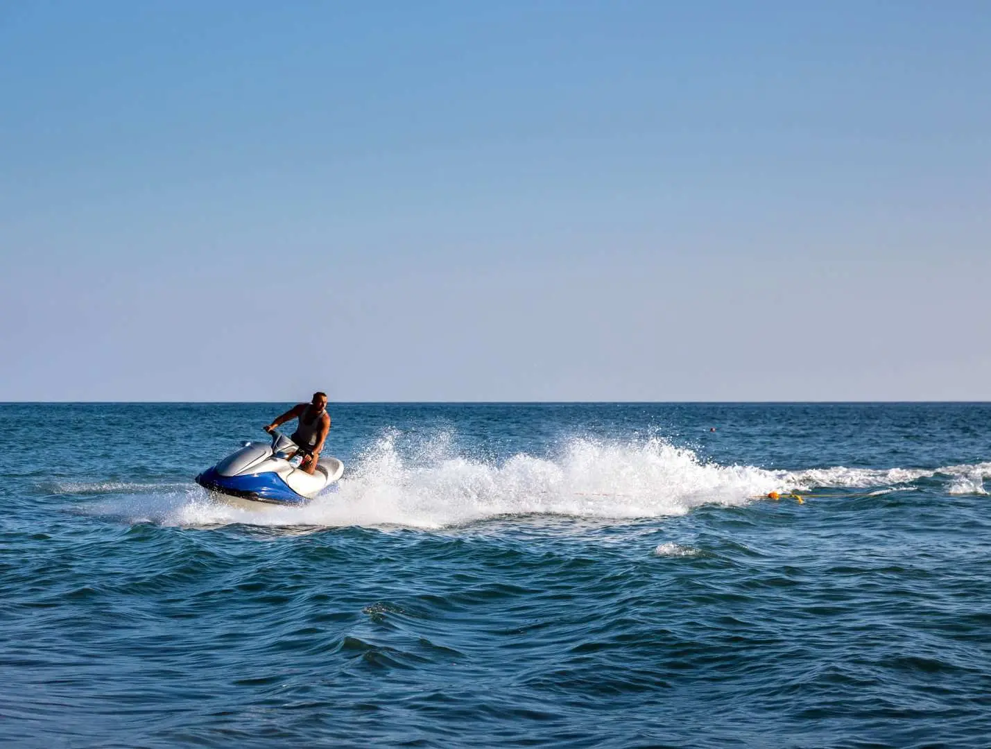 A tourist experiencing the thrill of jet skiing on the azure waters near Koh Larn, Pattaya, leaving a white wake, enjoying an exciting marine sport activity.