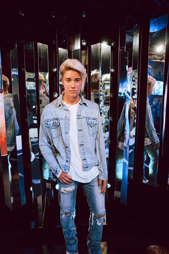 Justin Bieber's wax figure at Madame Tussauds Bangkok, dressed in stylish denim, standing in front of mirrored walls that create dynamic reflections, highlighting the pop star's iconic look.