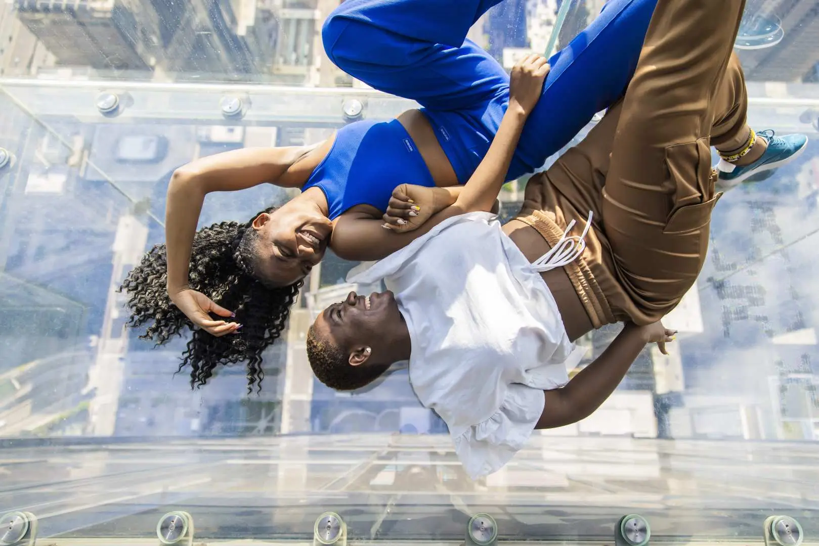 Two friends playfully posing on The Ledge's transparent glass floor at Skydeck Chicago, bravely looking down at the spectacular Chicago city below.