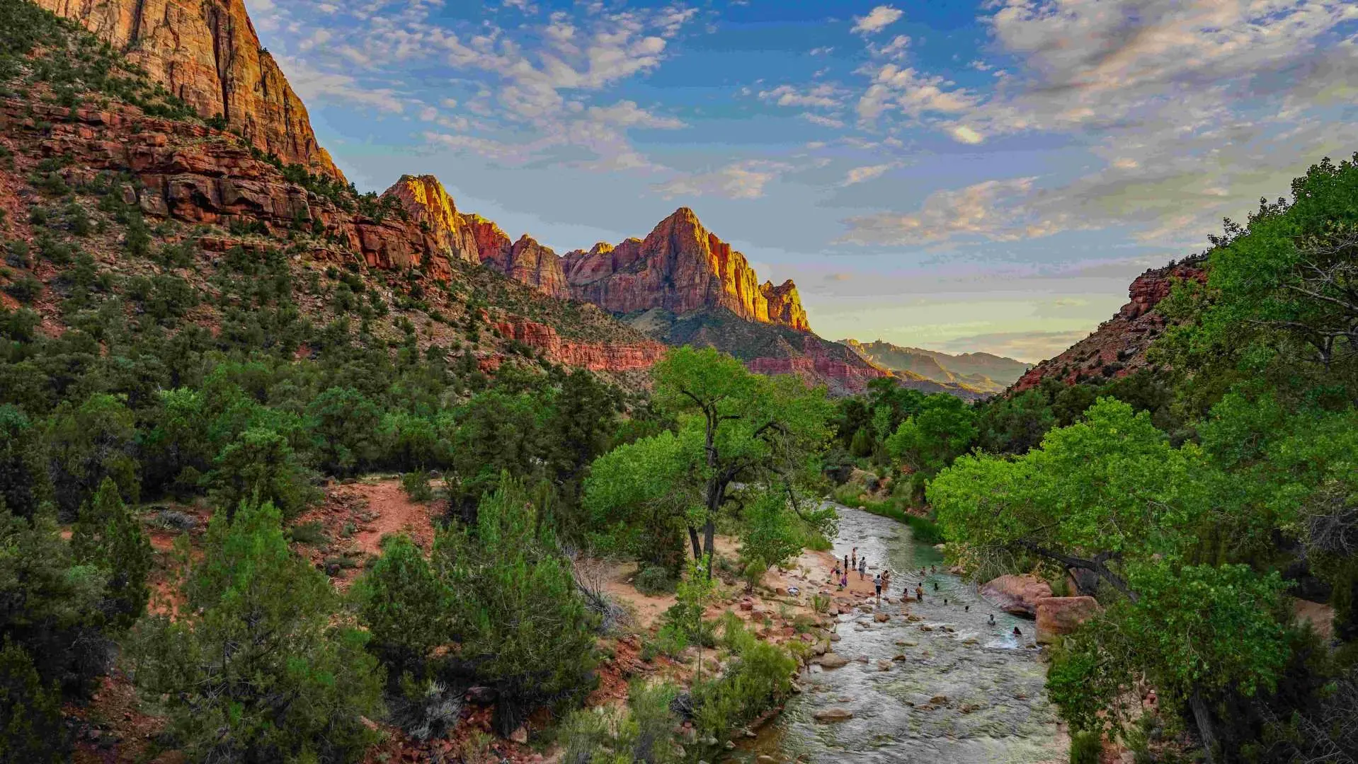 Serene landscape of Zion National Park, featuring a gentle river flowing through a lush green valley, framed by majestic red rock mountains at sunset, experiencing Utah's natural majesty.
