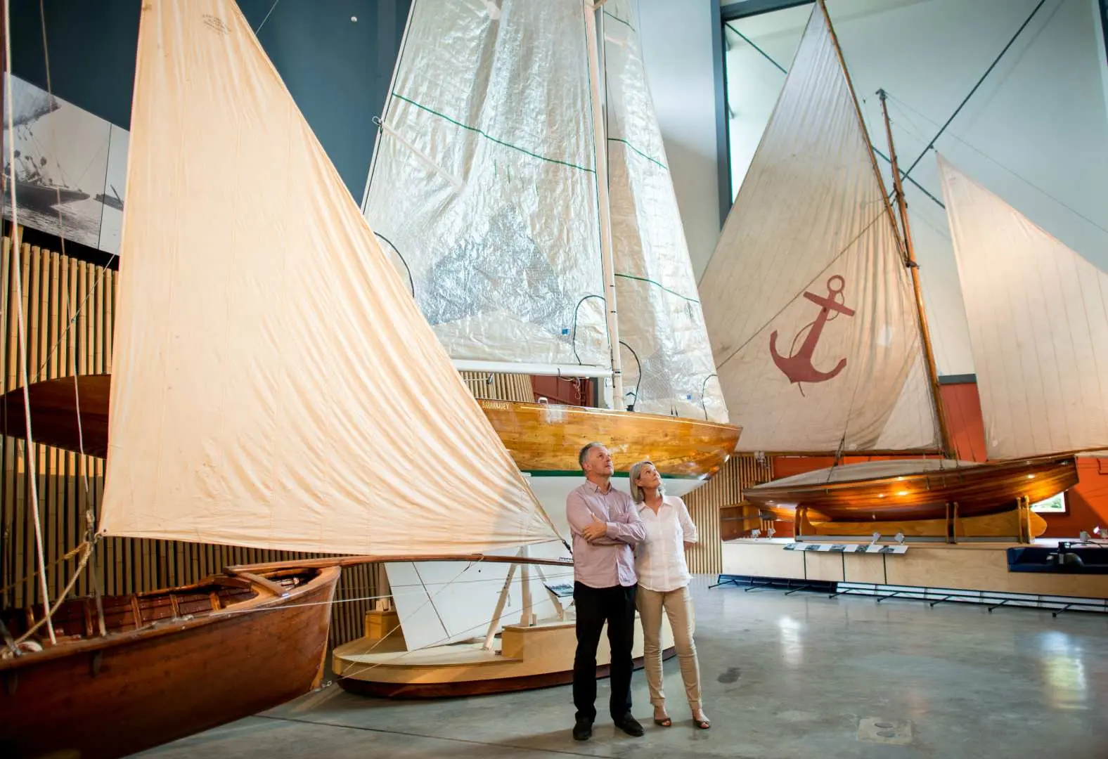 Two visitors exploring the spacious indoor exhibition hall at the Australian National Maritime Museum, admiring various historical sailing boats and ship models, delving into Australia's rich maritime collection.