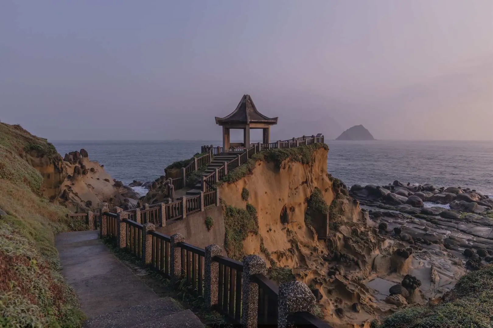 和平島地質公園崖邊的古樸涼亭，階梯蜿蜒而上，在柔和光線下遠眺平靜大海與遠方基隆嶼，氛圍靜謐。
