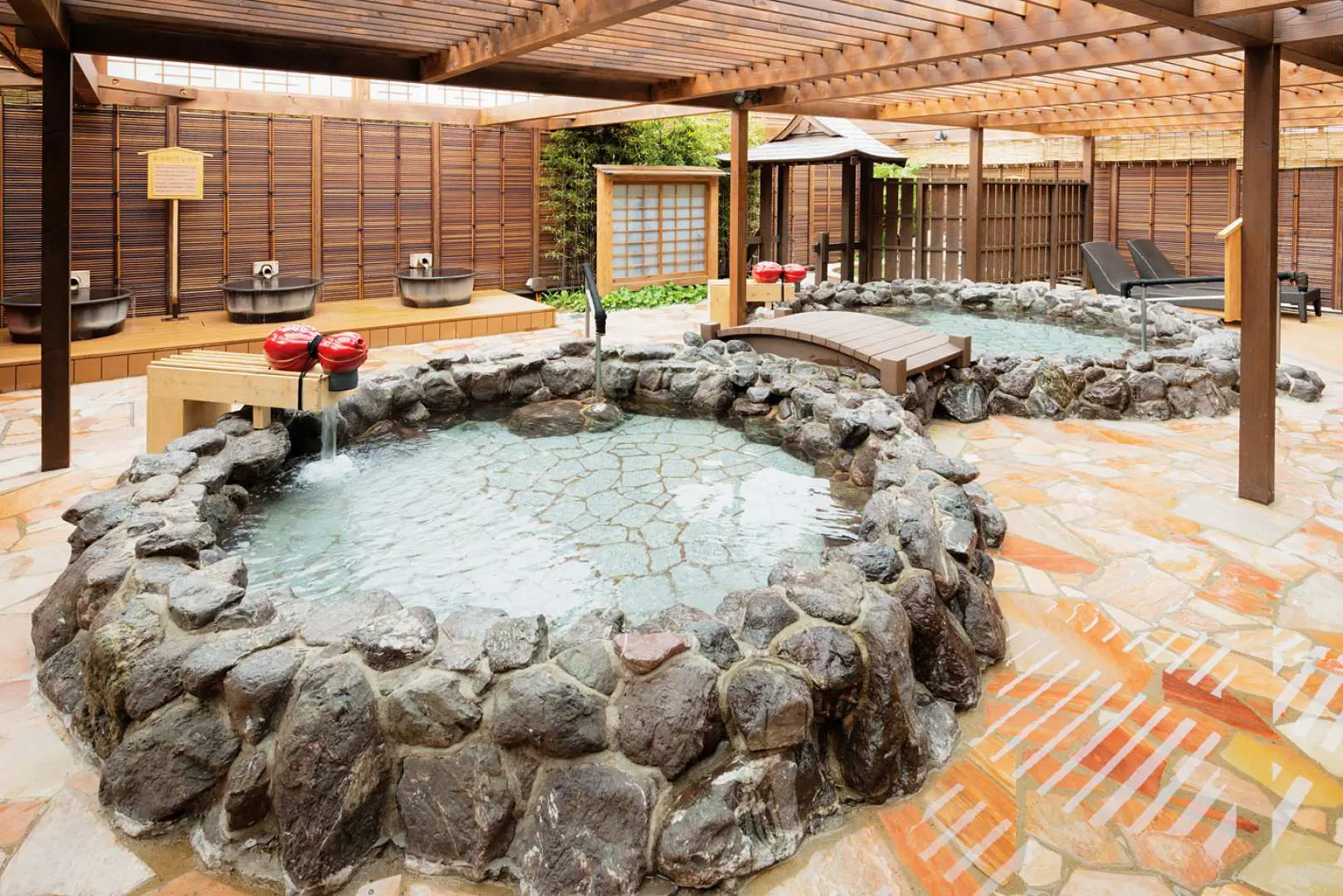 Spacious and comfortable open-air hot spring area at Arima Onsen Taikou no Yu, featuring multiple stone-built baths under a wooden roof for an outdoor bathing experience.