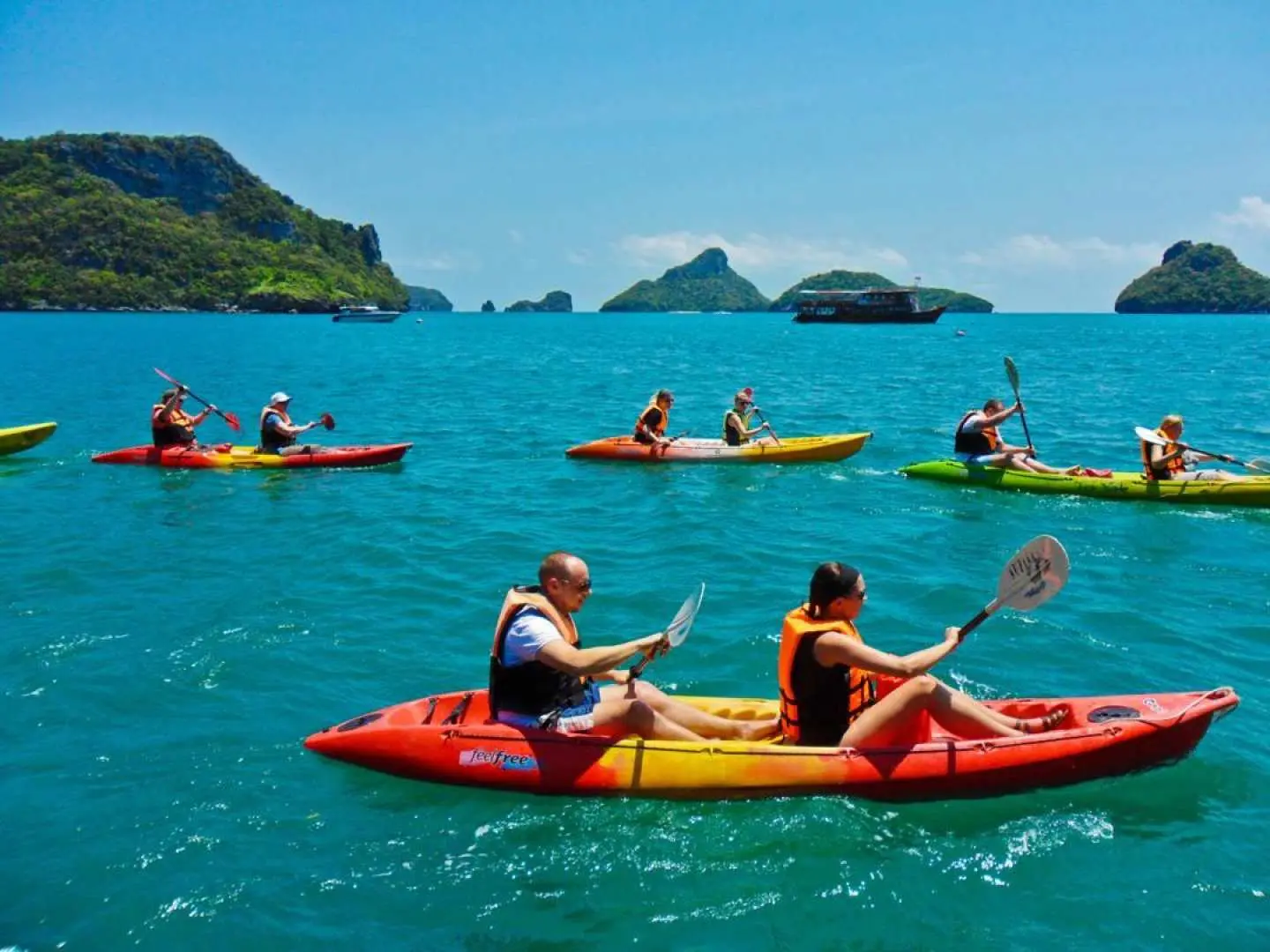 Multiple visitors enjoying a kayaking experience in the clear blue waters of Angthong National Marine Park near Koh Samui, paddling between lush green islands under a sunny sky.