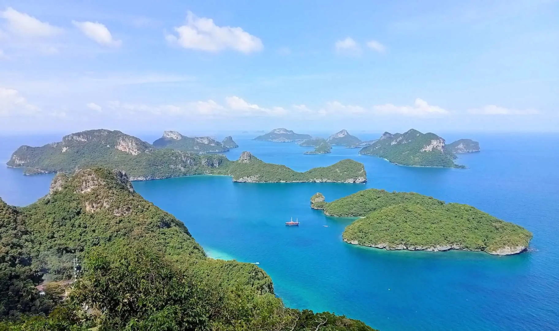 A breathtaking panoramic view of Angthong National Marine Park in Koh Samui, with numerous lush green limestone islands scattered across the vast blue ocean, a tour boat gently cruising.