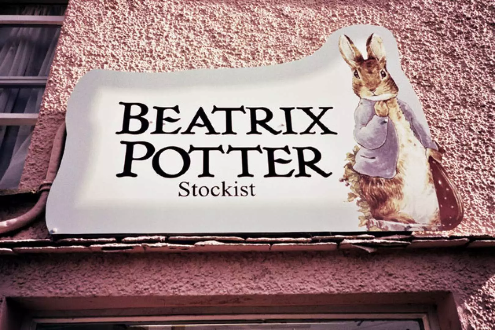 A sign for 'Beatrix Potter Stockist' featuring an illustration of Peter Rabbit, indicating a location related to the famous author in the Lake District, such as Lindeth Howe Country Hotel for afternoon tea.