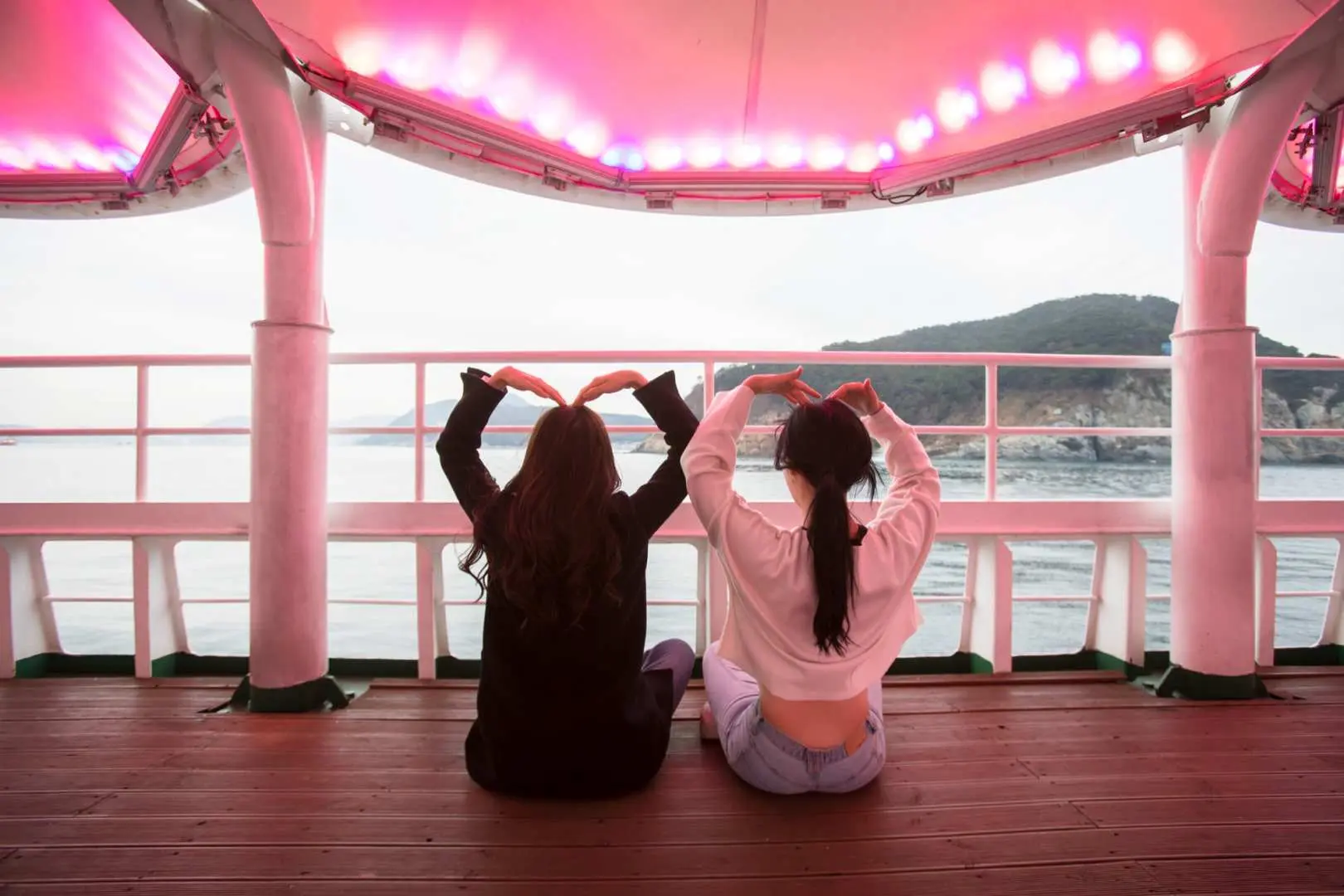 Hai du khách trên boong du thuyền Jagalchi Busan được trang trí đèn hồng, quay lưng tạo dáng trái tim, tạo nên những kỷ niệm đêm lãng mạn.