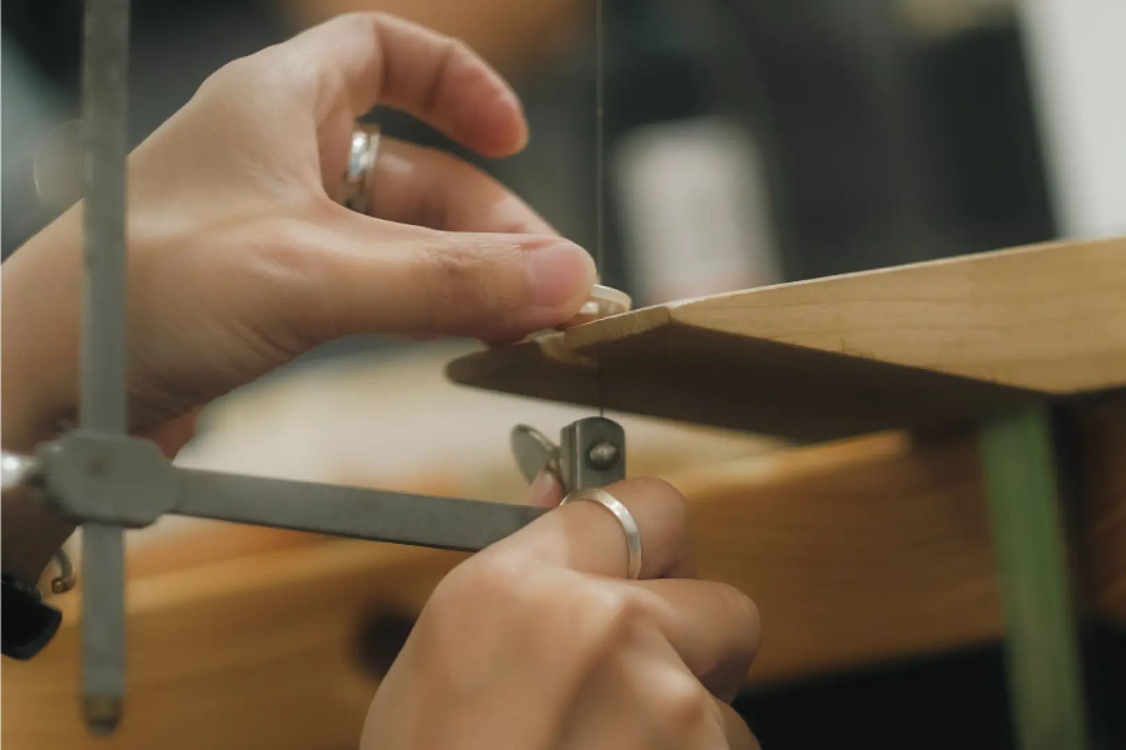 A participant in a Chiayi handmade silver jewelry workshop carefully operates a jeweler's saw, precisely cutting silver material under expert guidance to master metalworking techniques.