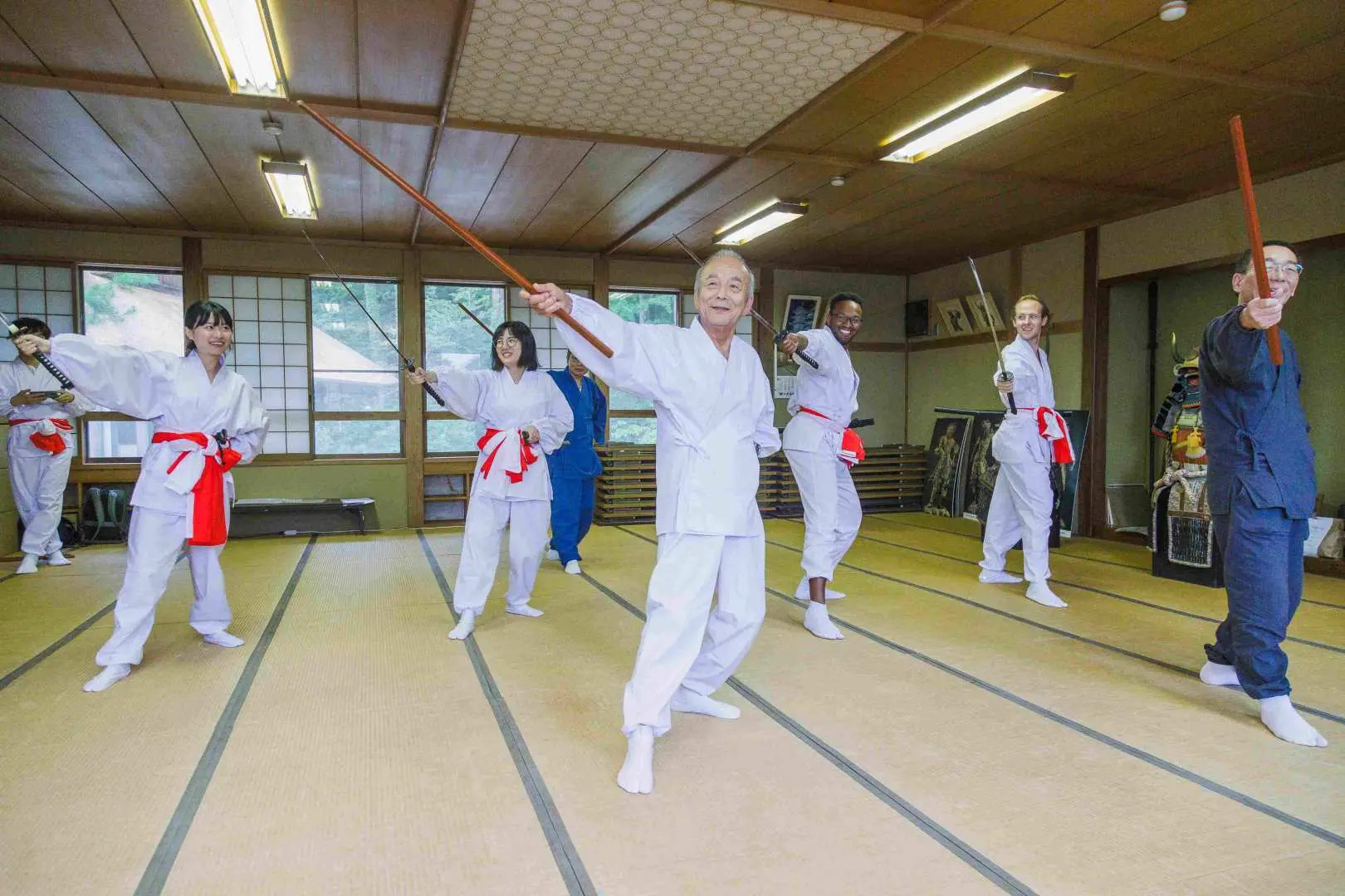 Participants at Yamagata's Jionji Temple spiritual training experience, dressed in white robes, practice martial arts or spiritual discipline with wooden staffs, embracing traditional Shugendo culture.