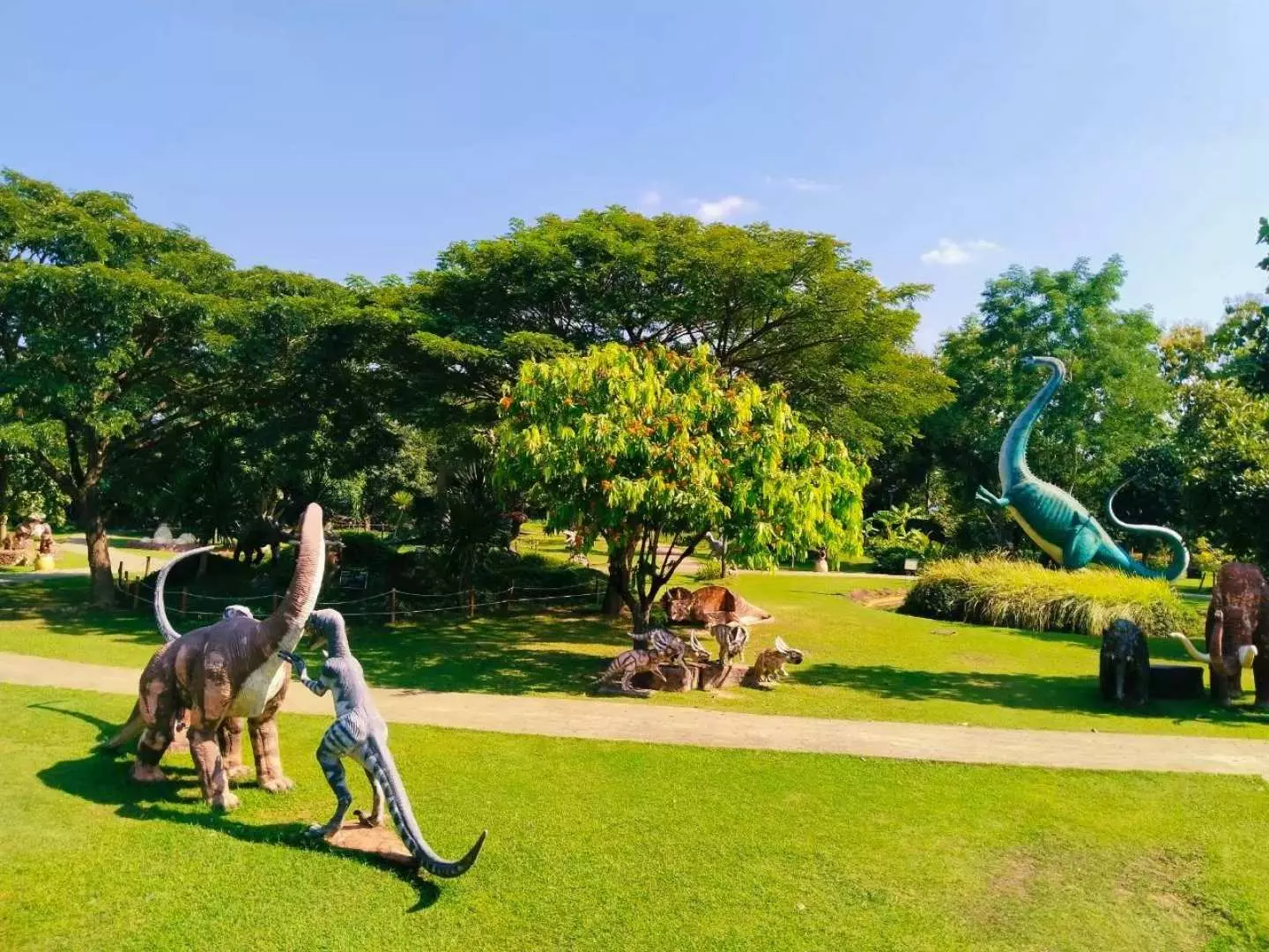 A panoramic view of Chiang Mai Hidden Village's vast dinosaur park, with various dinosaur sculptures scattered across green lawns and winding paths, offering an immersive fantasy outdoor adventure.
