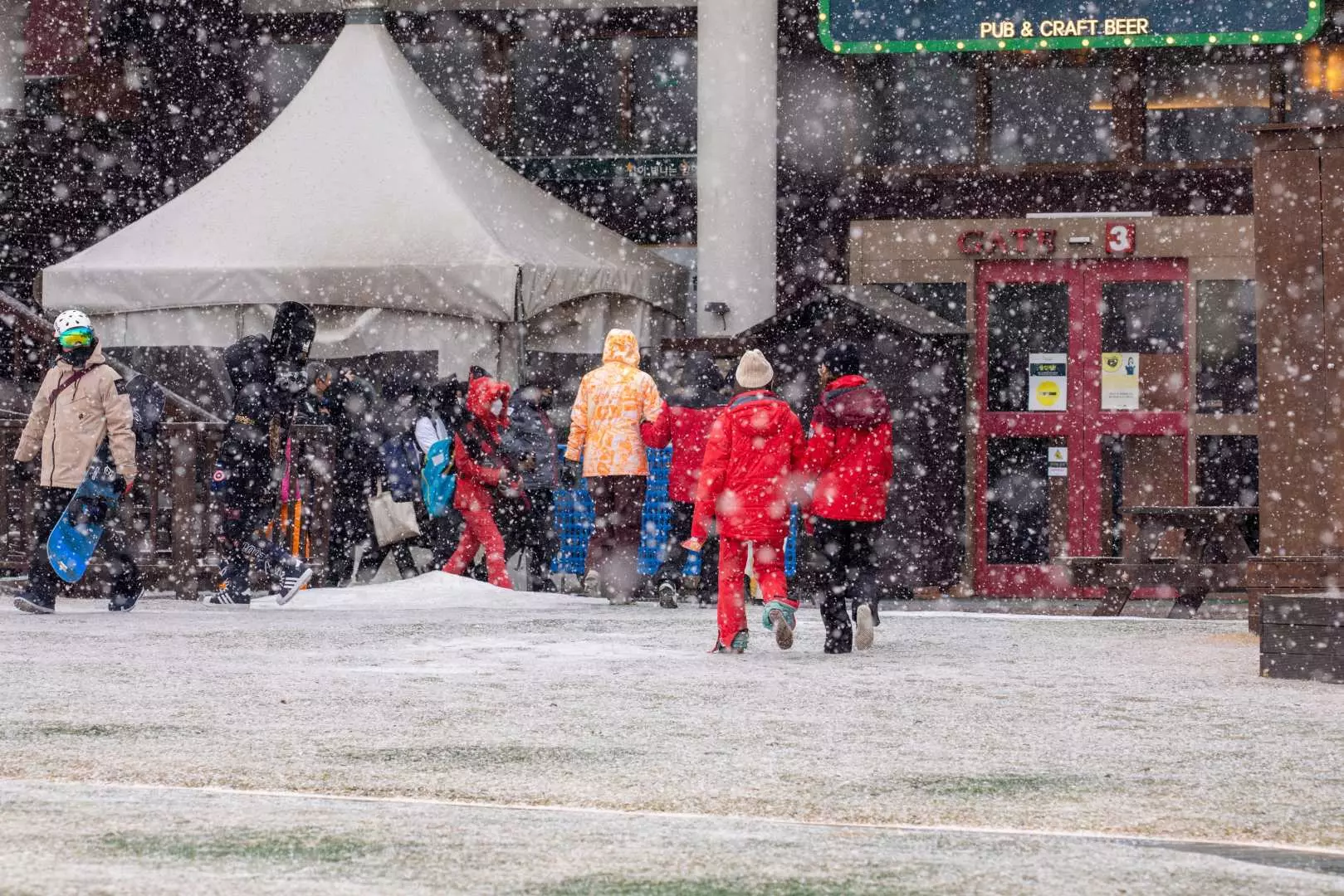 江原道龍平度假村，戶外廣場上雪花紛飛，遊客們穿著鮮豔的冬季服飾漫步，感受濃厚的節慶氣息與冬季魅力。