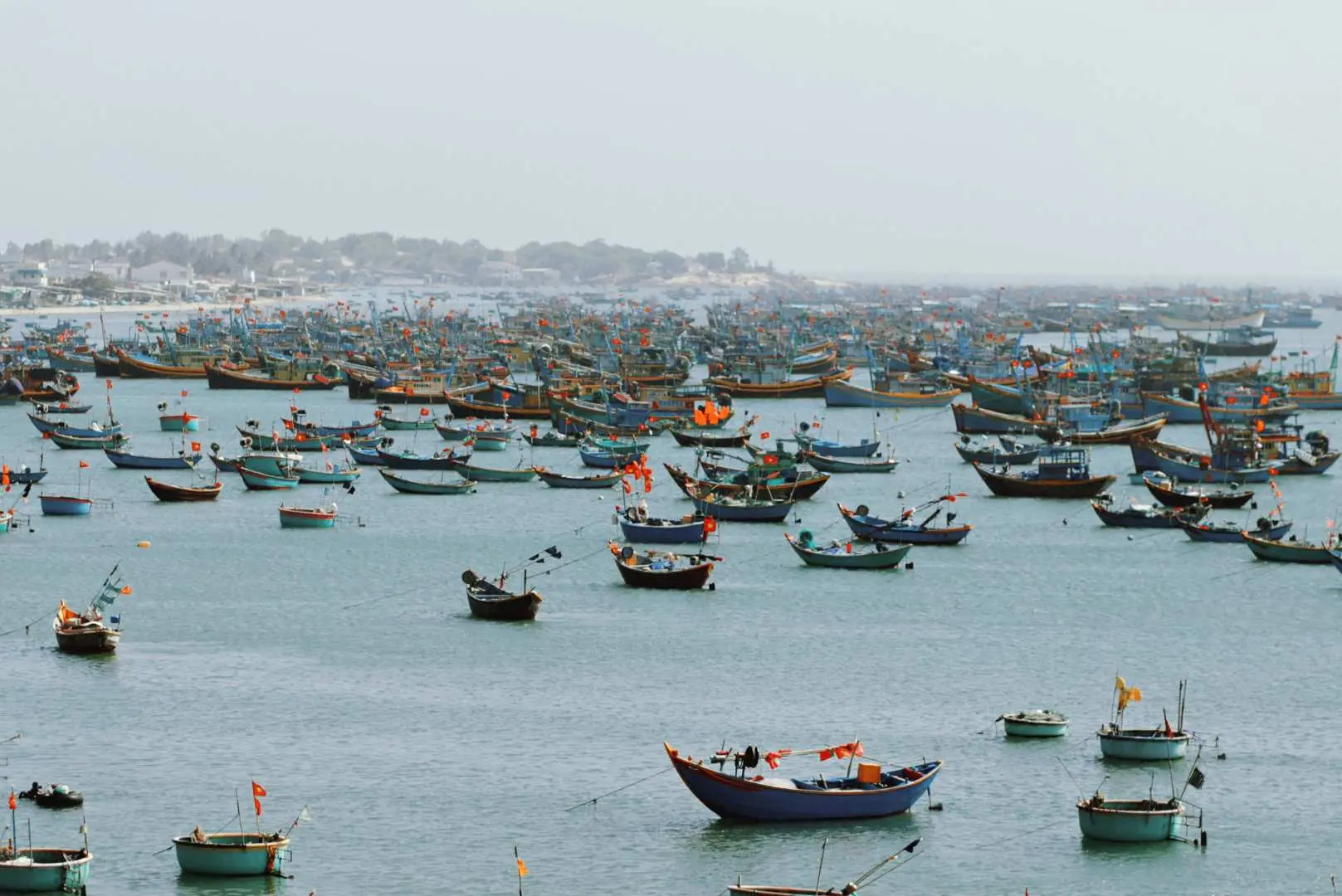 Khung cảnh toàn cảnh tuyệt đẹp của làng chài Mũi Né nhộn nhịp, với hàng trăm chiếc thuyền truyền thống Việt Nam đầy màu sắc neo đậu trong vịnh yên bình, phản ánh cuộc sống và văn hóa địa phương.