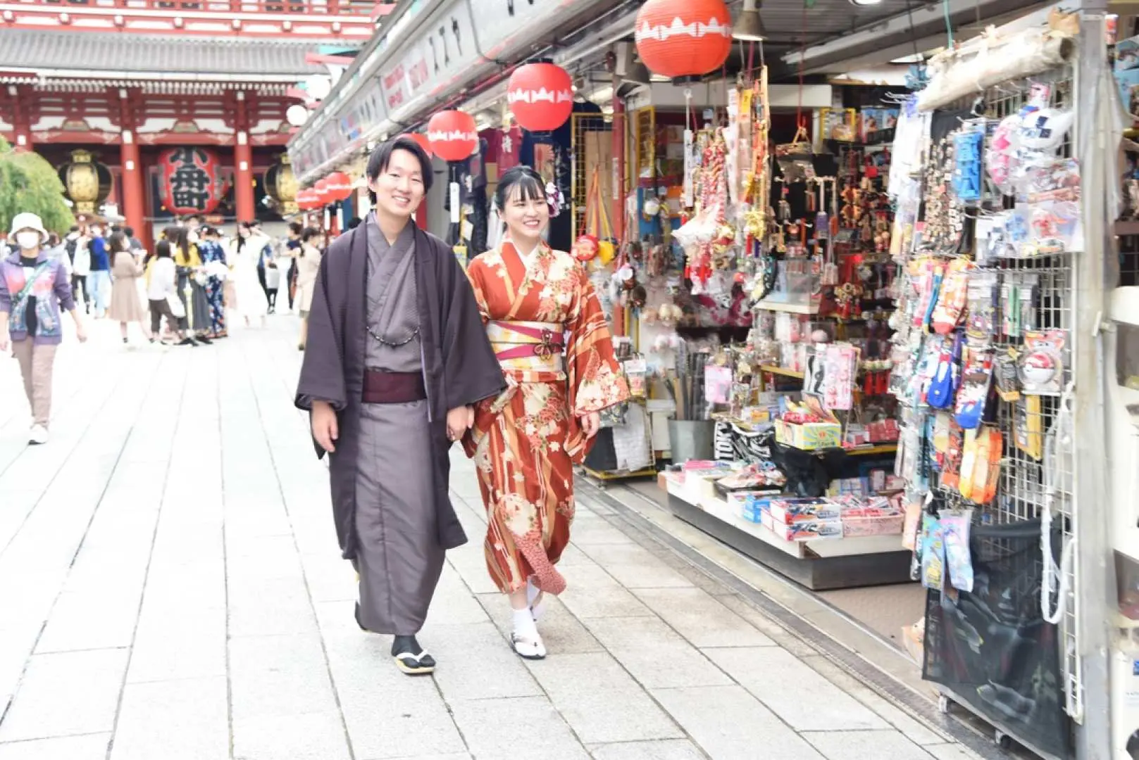 東京浅草の雷門商店街を和服姿のカップルが手をつないで散策する様子。浅草寺を背景に日本の文化体験を楽しんでいます。