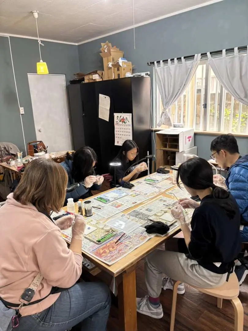 於沖繩金繼體驗工作坊中，幾位參與者圍繞著一張大檯，每個人都專心致志地製作他們的金繼作品。
