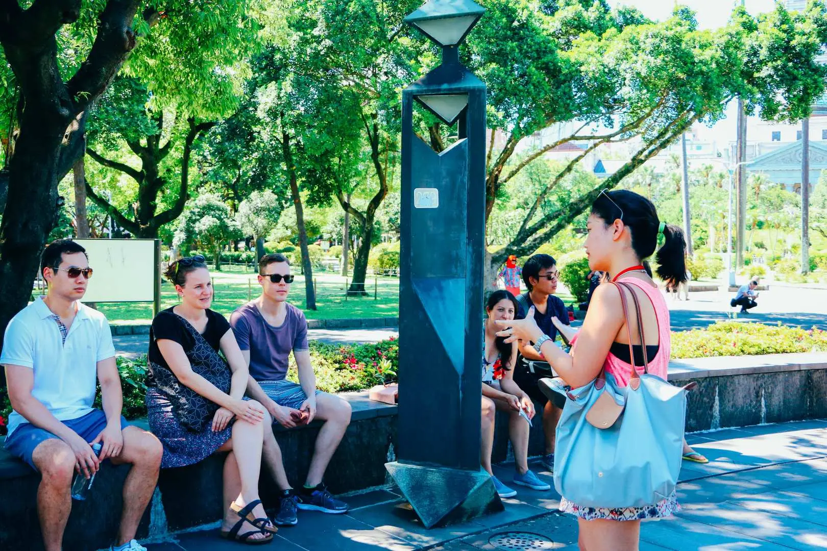 台北舊城區徒步導覽，遊客們在綠樹成蔭的公園中休憩，專心聆聽專業英語導遊講解台北的歷史與文化。