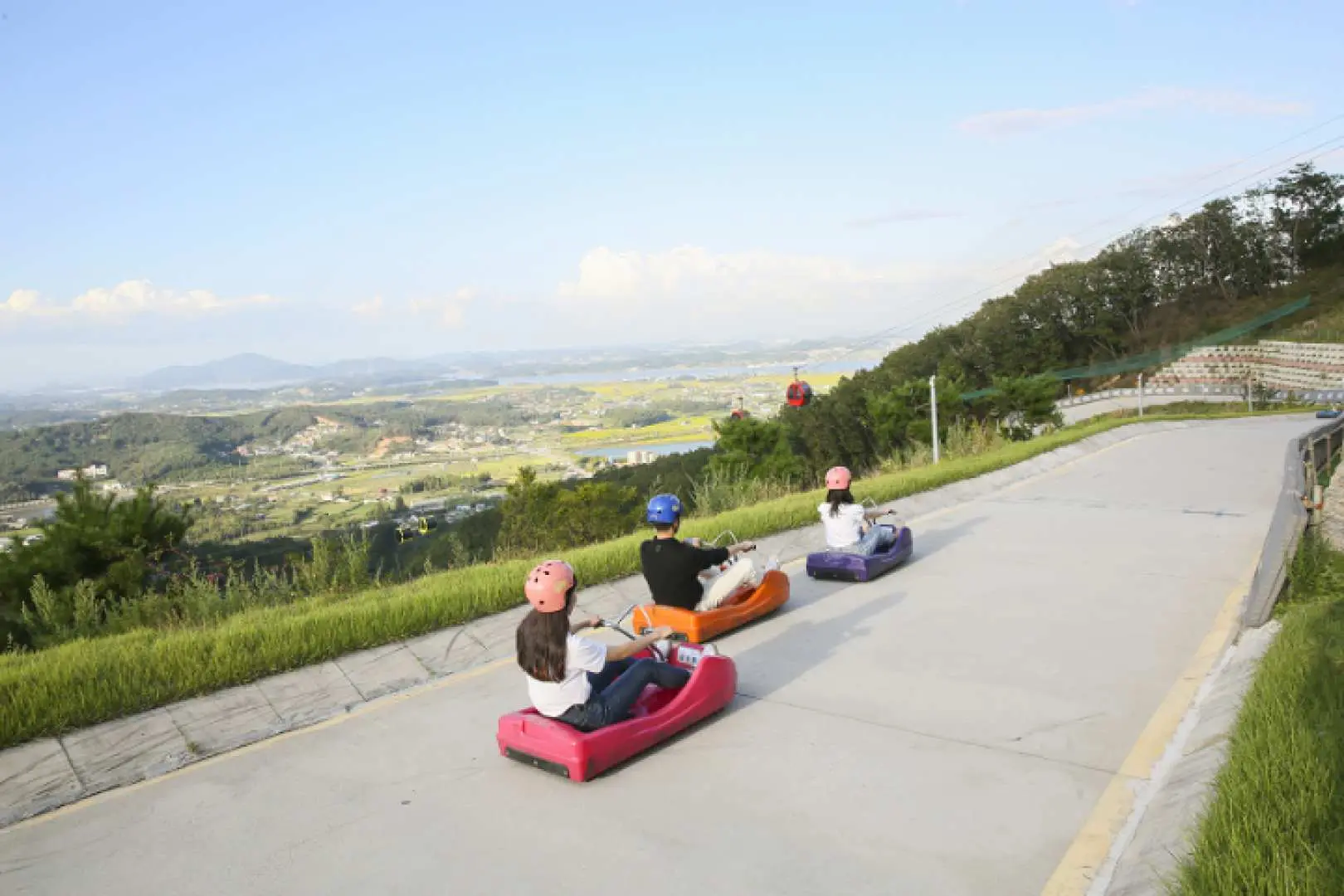游客在江华岛Luge斜坡滑车赛道上高速滑行，背景是开阔的仁川江华岛自然风光，体验刺激与美景。