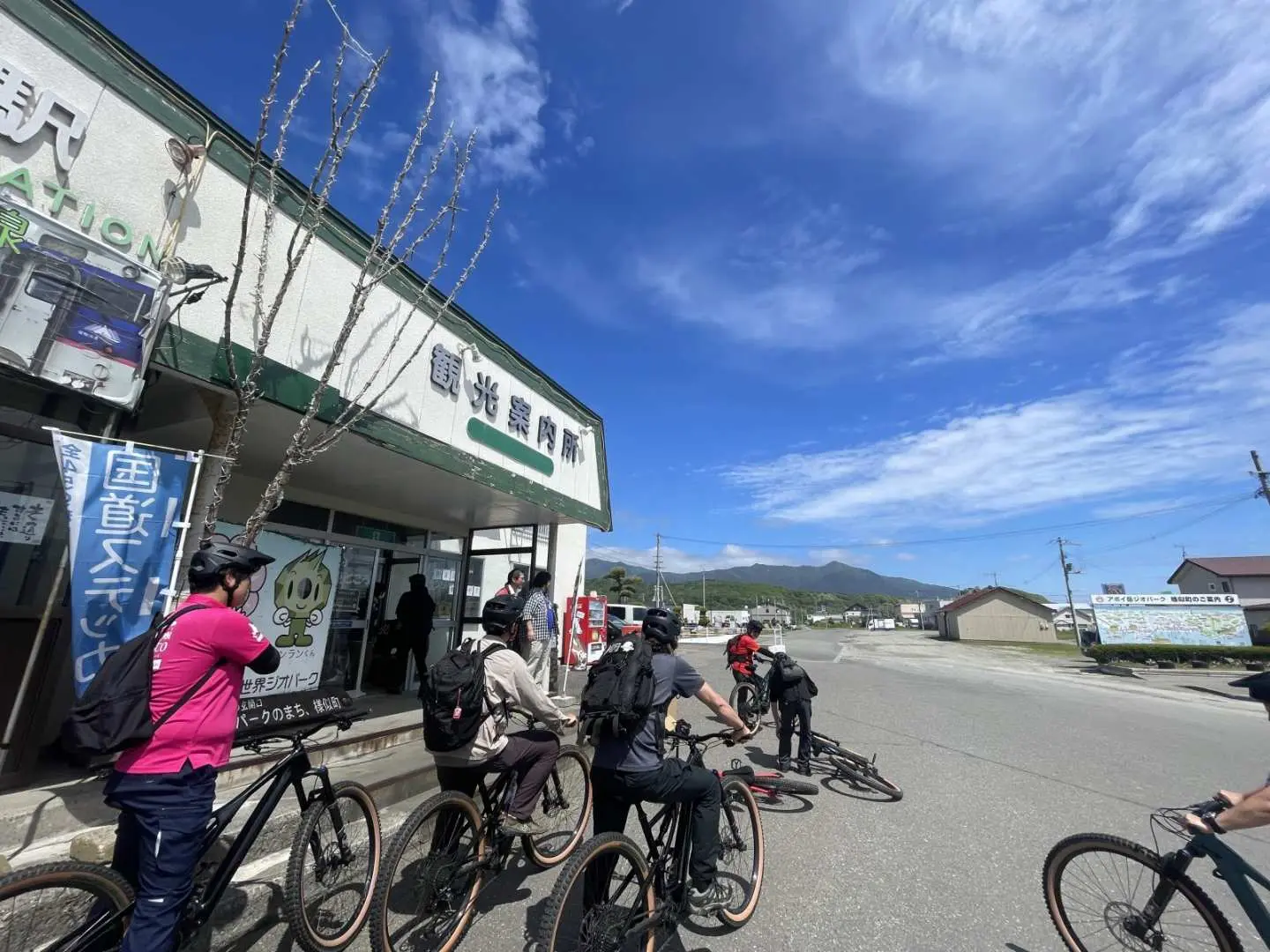體驗者在北海道樣似町的小鎮上，騎乘電動登山車，於當地建築前集合，準備開始悠閒的山麓探險，感受純樸的當地生活與文化。