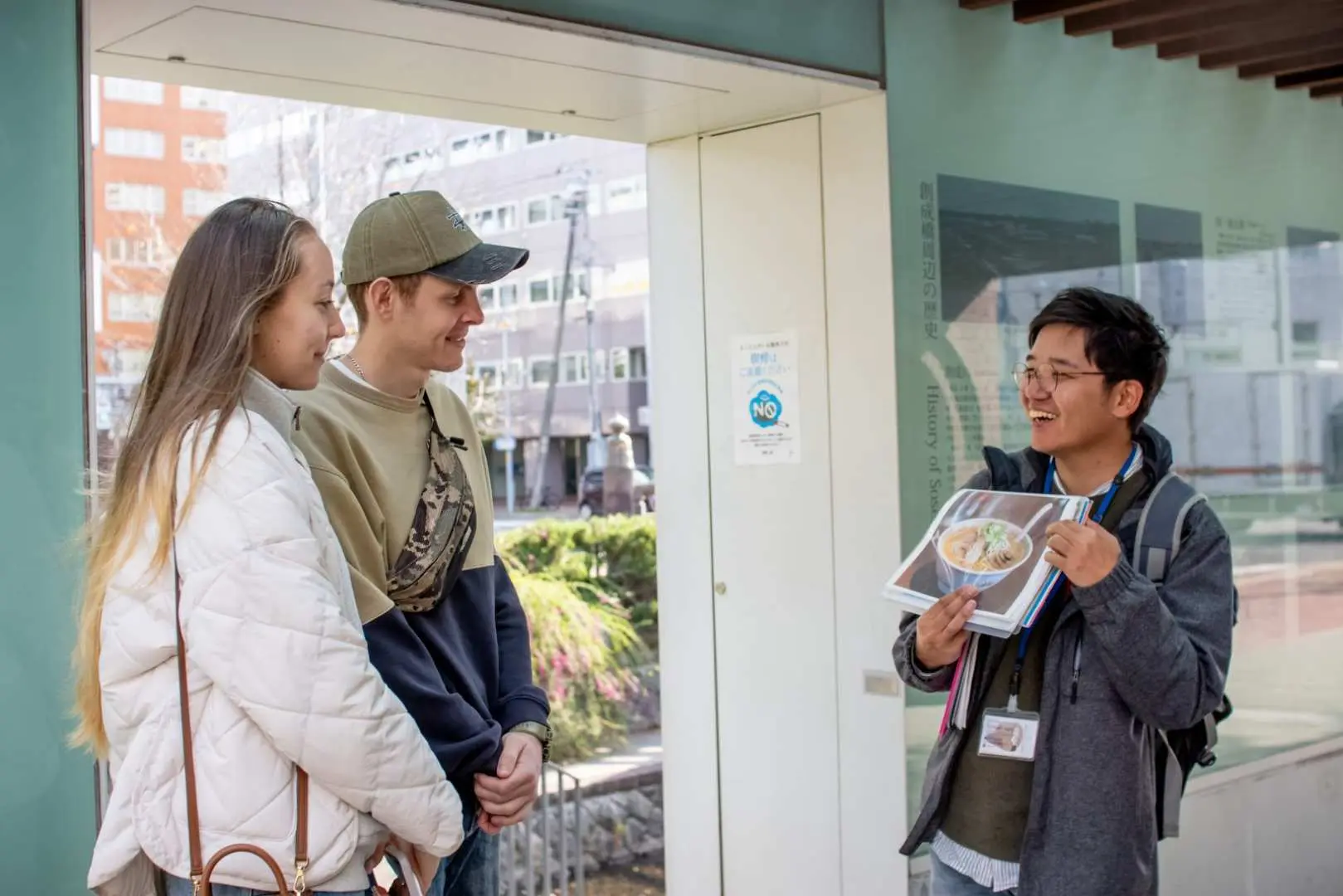 A private Sapporo guide shows ramen pictures to two visitors, explaining the background and culture of ramen in detail, adding depth and anticipation to the upcoming culinary experience.