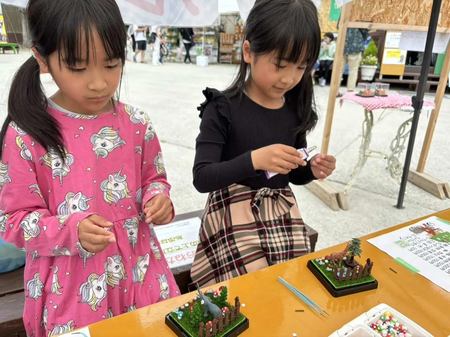 日本の白鳥動物園が提供する様々な親子体験活動。二人の女の子が屋外テーブルで動物テーマの手作りを楽しんでいます。