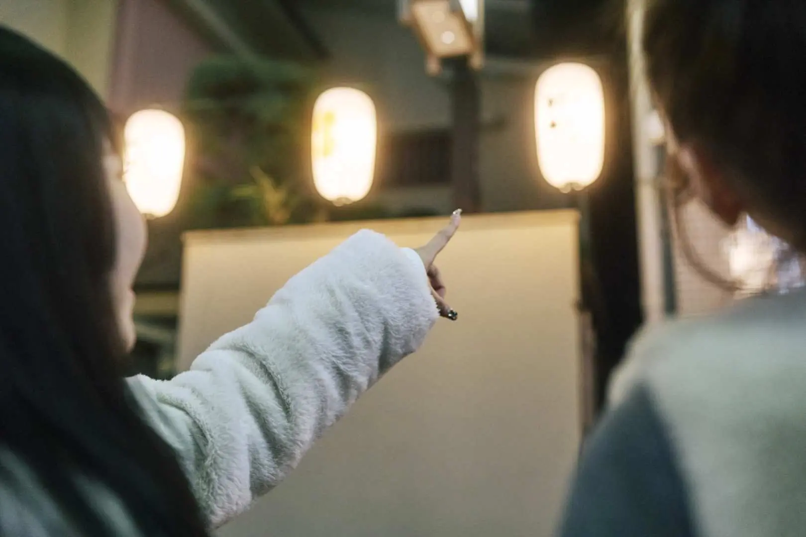 A tourist pointing at traditional Japanese paper lanterns illuminating the charming night streets of Daimoncho, Mito, highlighting the unique ambiance.