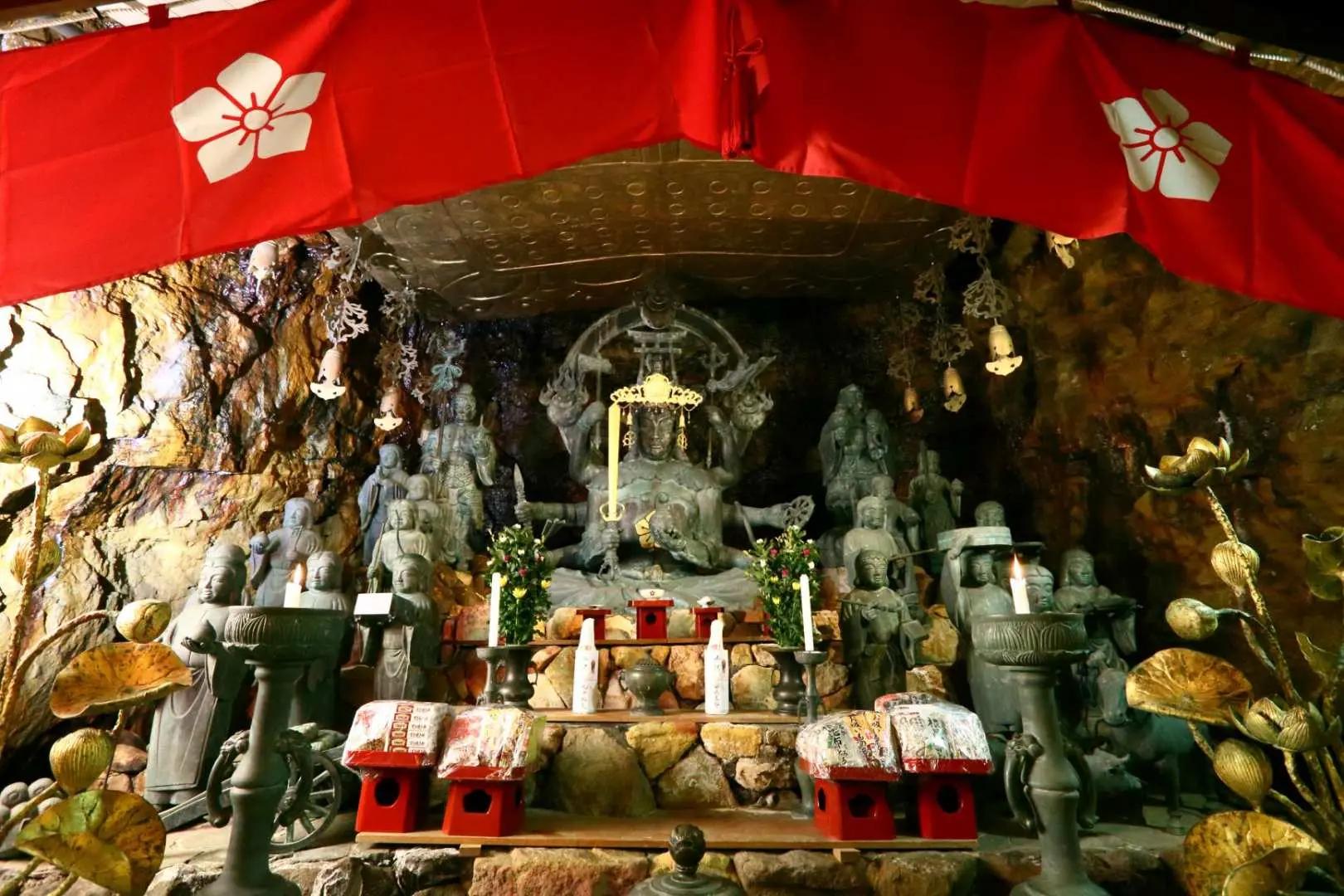 An ancient shrine inside Sandanbeki Cave, housing solemn statues, with red drapes and candles creating a dignified and mysterious historical atmosphere.