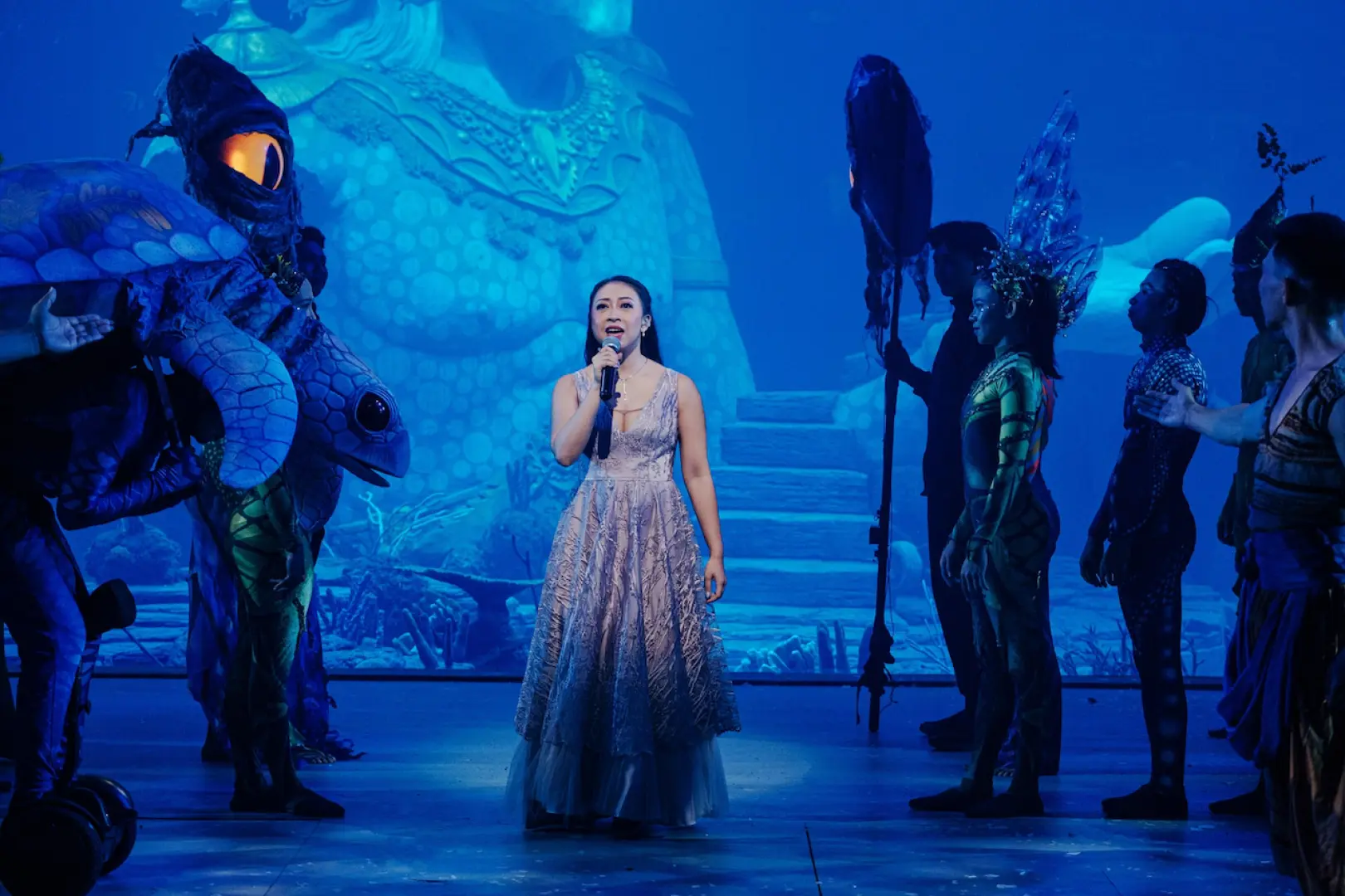 A singer performs center stage at the Varuna Show, surrounded by dancers in magnificent marine creature costumes, highlighting Bali's unique underwater theatrical charm.
