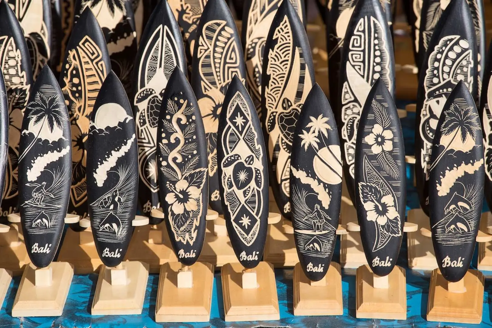 Rows of intricately carved wooden surfboard souvenirs are displayed at Bali's Toko Oleh Oleh Dewata shop, showcasing unique Balinese culture and perfect for purchasing local handicrafts.
