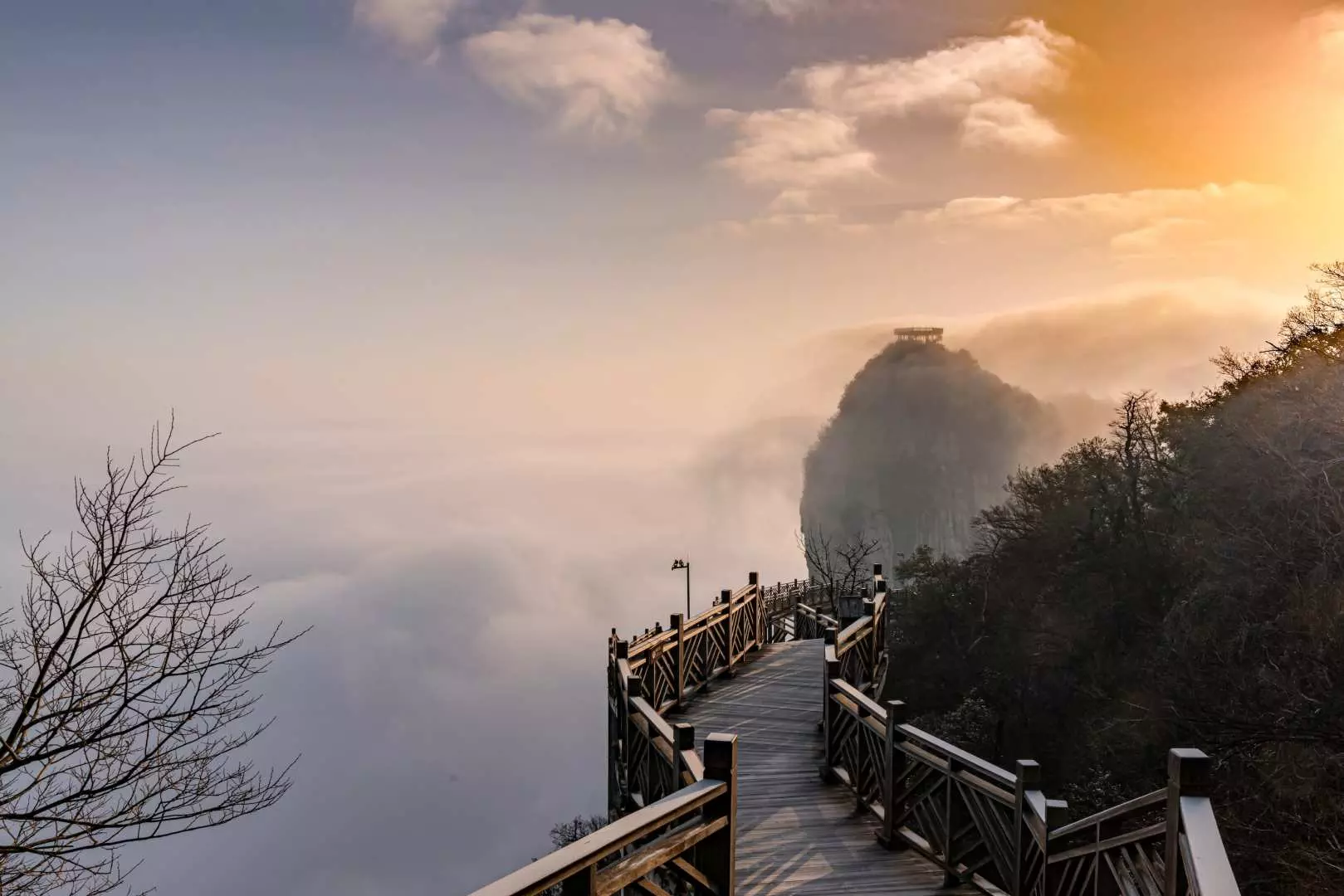 The Guigu Plank Road on Tianmen Mountain extending above a vast sea of clouds, with soft golden sunlight piercing through, creating a breathtaking, ethereal wonderland scene.