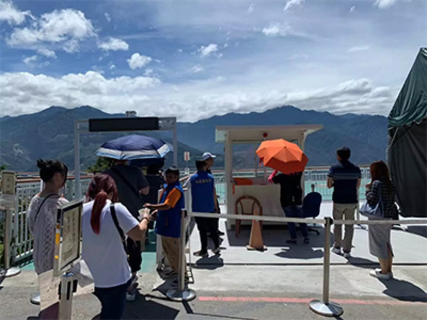 清境農場高空景觀步道的戶外驗票口，工作人員引導遊客掃描電子票券入園，遠處群山環繞，天氣晴朗宜人。