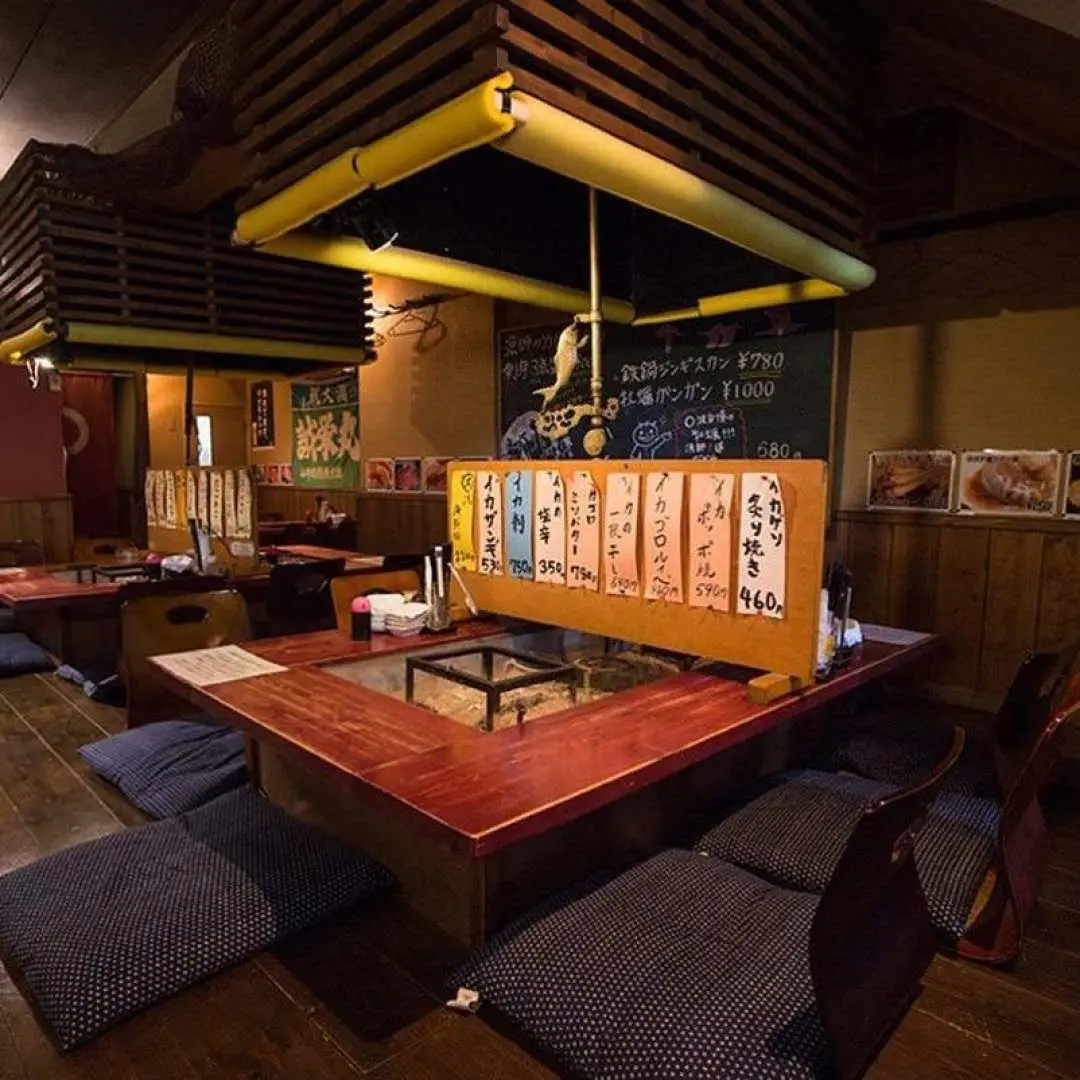 Inside a traditional Hakodate seafood robatayaki restaurant featuring an Irori hearth, where guests enjoy local delicacies and an authentic Japanese dining atmosphere on the night tour.