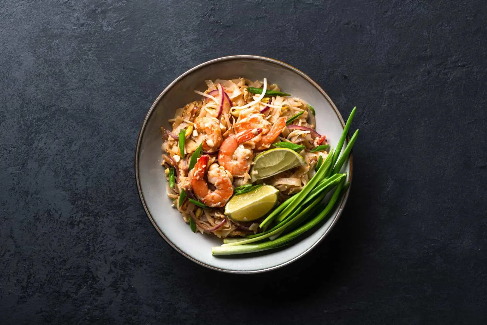 A beautifully plated bowl of authentic Pad Thai, complete with fresh large prawns, lime, and aromatic spring onions, highlighting Bangkok's local flavor and rich ingredients.